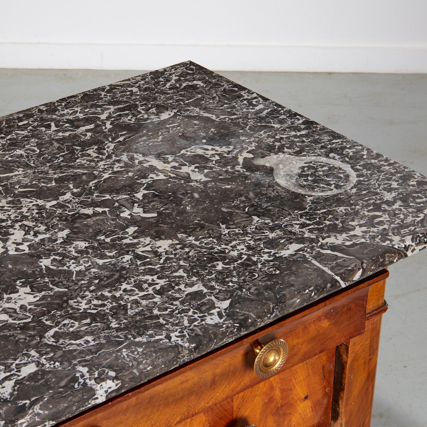 Classica commode in noce di Louis Philippe con un piano in marmo nero splendidamente variegato con angoli arrotondati che sovrasta quattro cassetti, ciascuno dotato di tiretti a rosetta in metallo dorato, scanalature a medaglione e una montatura