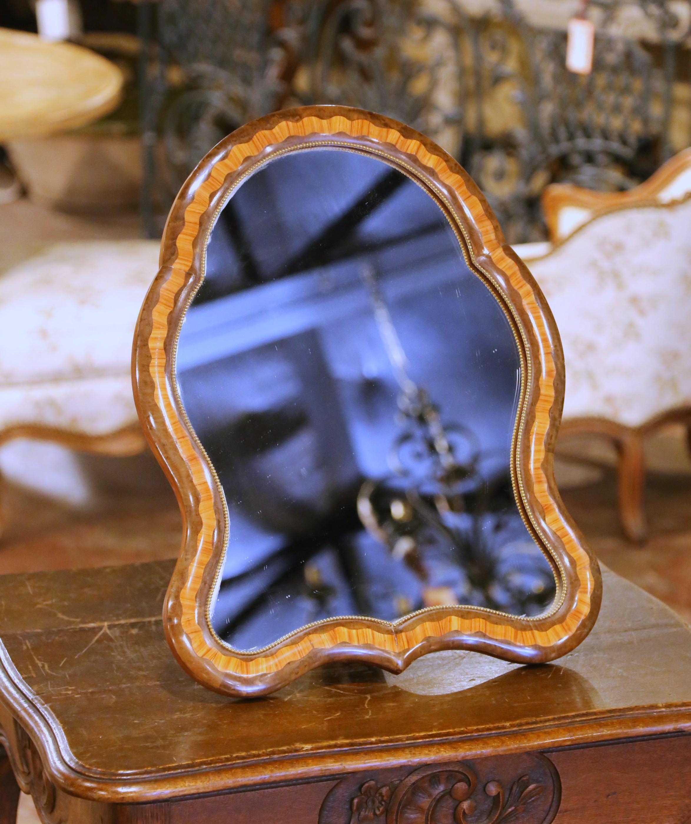 This antique French vanity mirror, crafted circa 1880, reflects the refined elegance of the Louis Philippe style with decorative touches influenced by the Napoleon III period. The shapely frame is veneered in warm walnut and features intricate