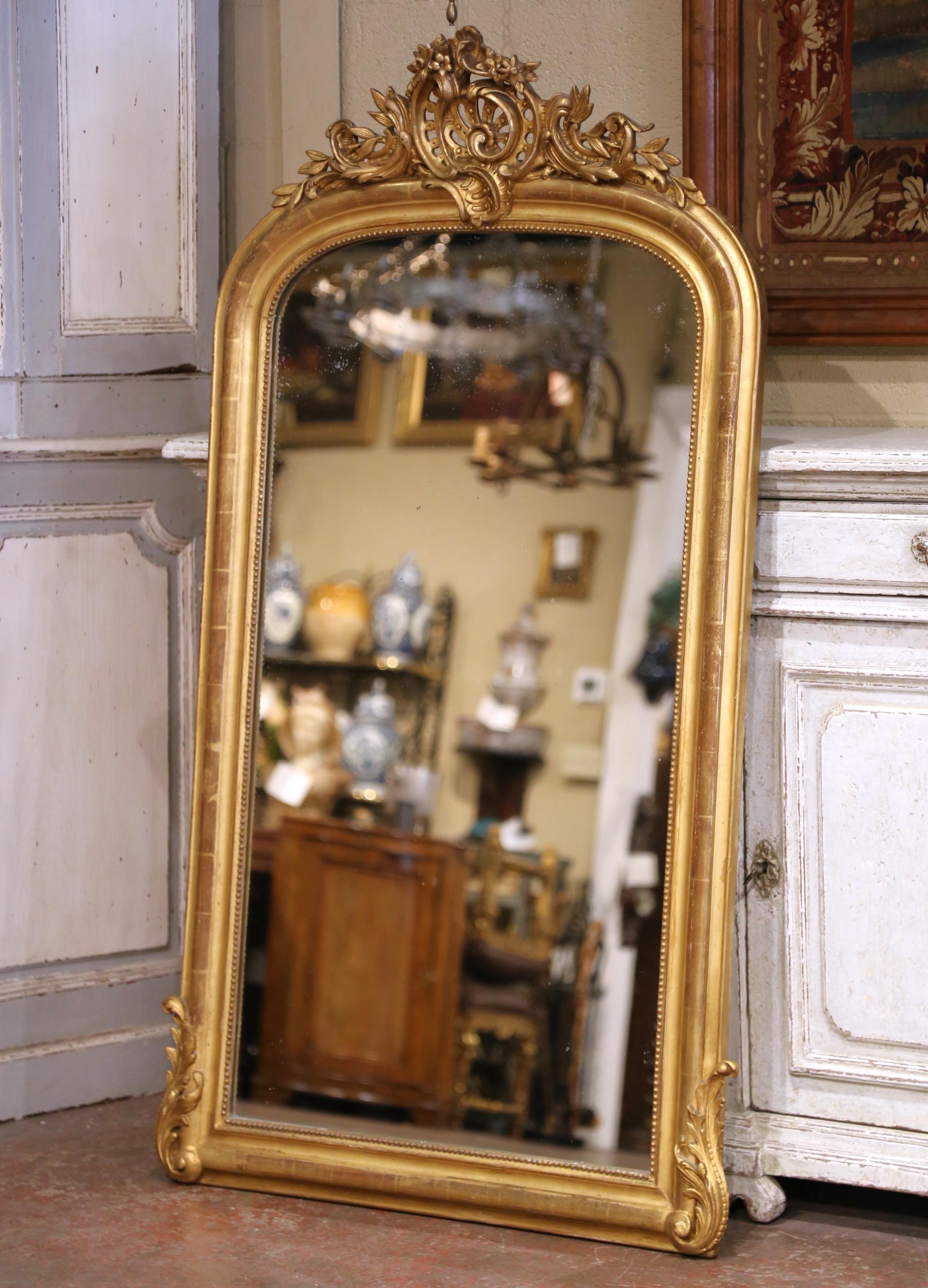 Ce miroir ancien de style Louis XV a été fabriqué vers 1870 et présente un cadre arqué en bois doré richement orné de sculptures rococo. Mesurant 61 pouces de haut, 32,75 pouces de large et 4,5 pouces de profondeur, le miroir attire l'attention par