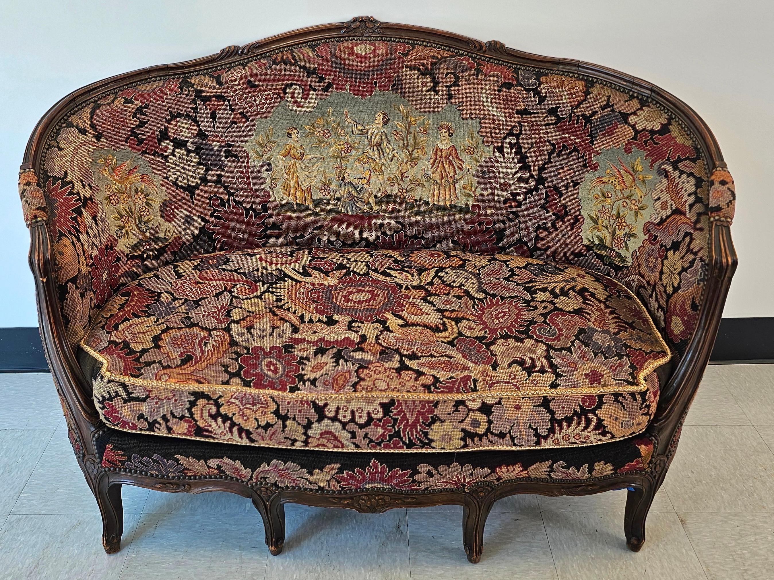 A French Louis XV style Settee features walnut frame with carved foliate, floral and scroll decoration; upholstered in pictorial needlepoint tapestry depicting courting scene in garden setting; 19th century.
Measures 55