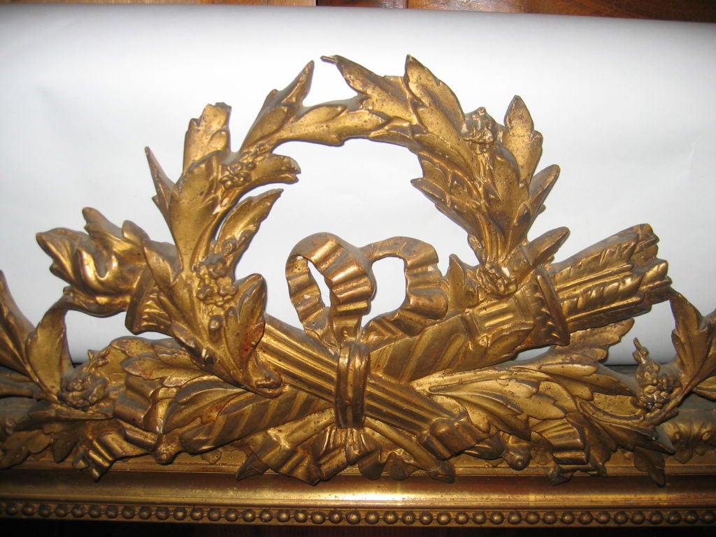 Miroir en bois doré de style Louis XVI du XIXe siècle. Verre original. Motif de torche et de carquois croisés, entouré d'une couronne de laurier.