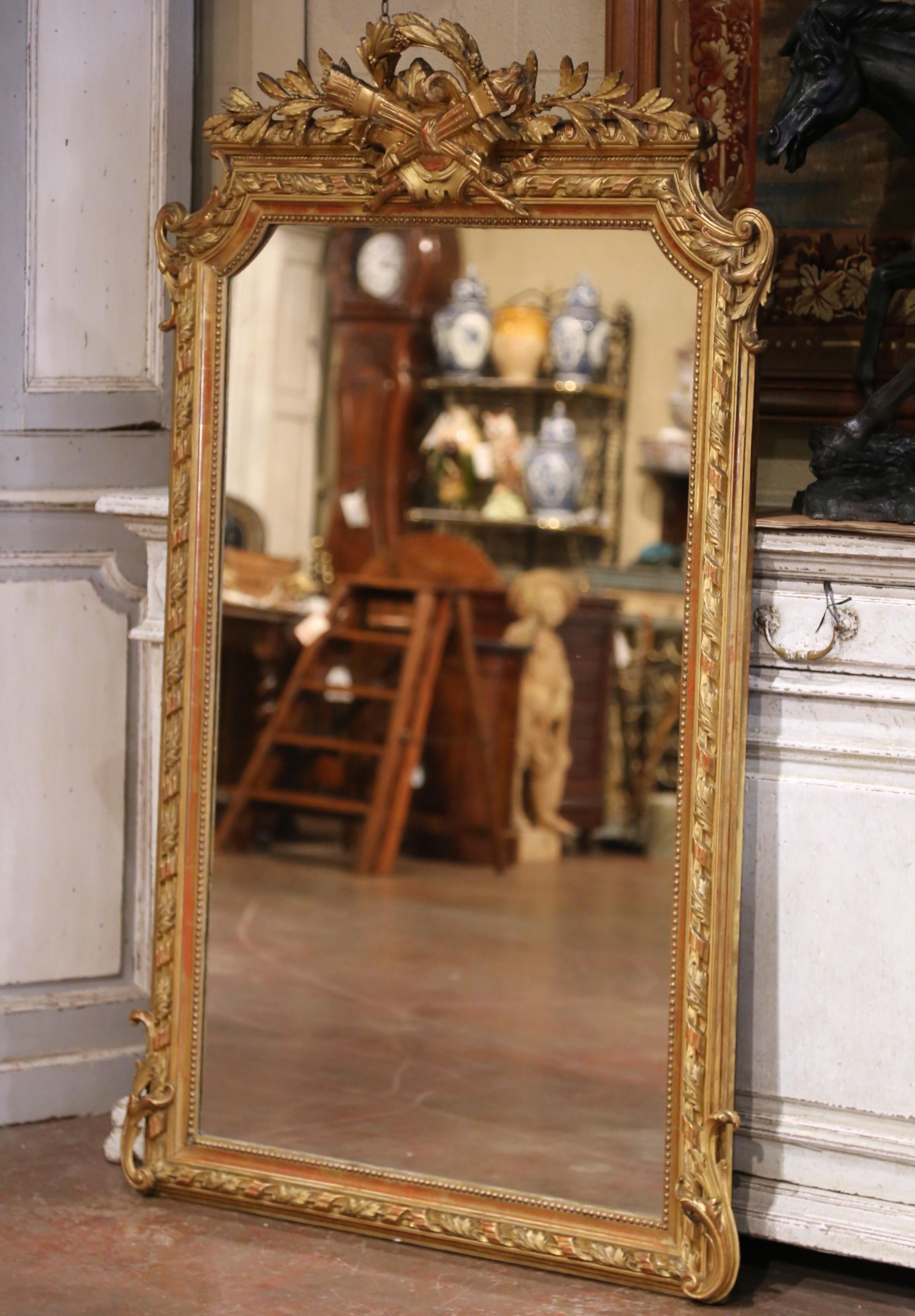 This elegant antique giltwood mirror was crafted in Paris, France circa 1870 in the Louis XVI style, celebrated for its neoclassical ornamentation and architectural symmetry. The crest features a finely carved laurel wreath tied with ribbon,