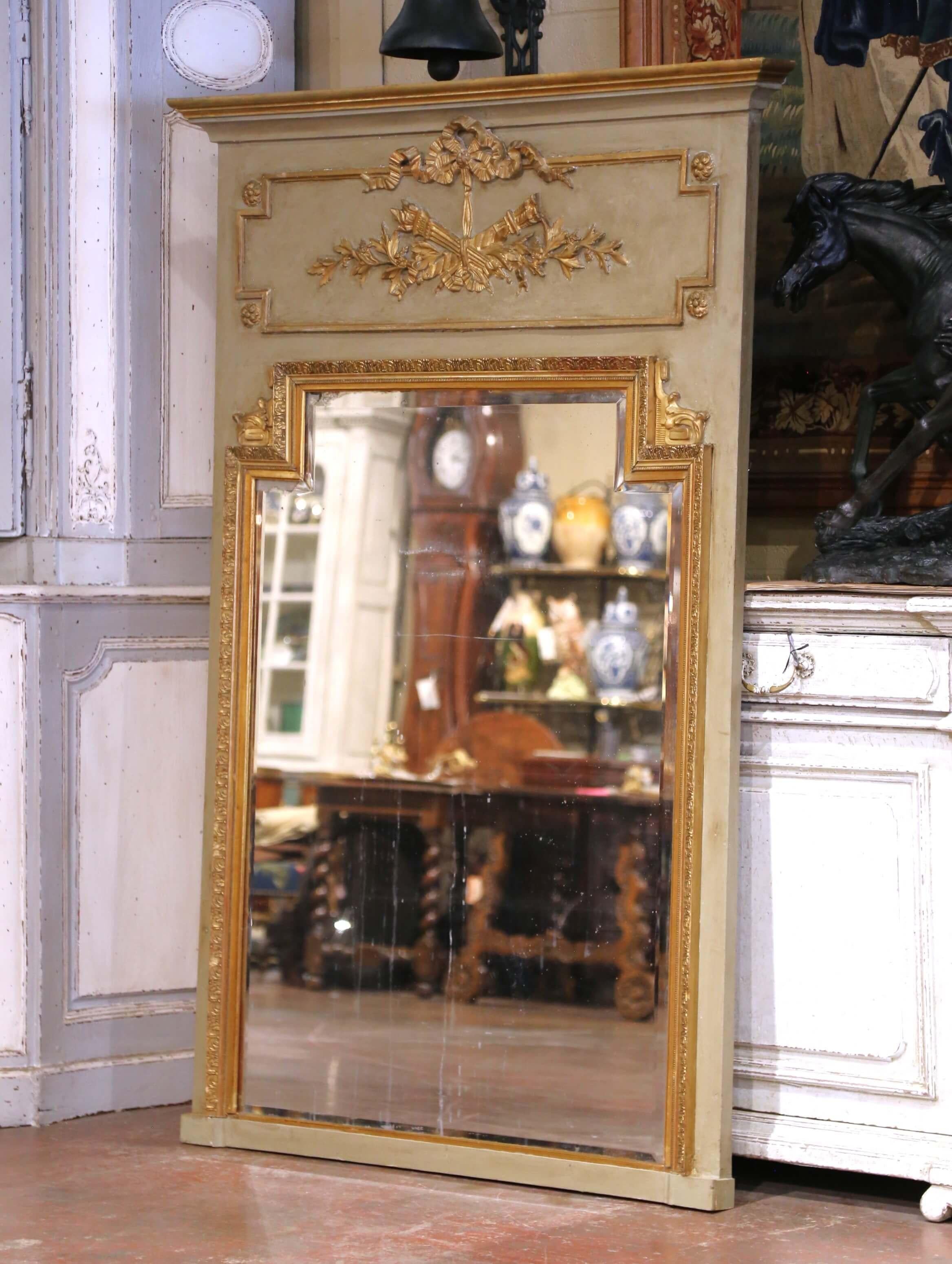 Fabriqué en France vers 1870, cet élégant miroir trumeau ancien illustre l'ornementation raffinée du style Louis XVI. Le cadre en bois peint et doré à la feuille est surmonté d'une composition classique en bas-relief représentant des flambeaux