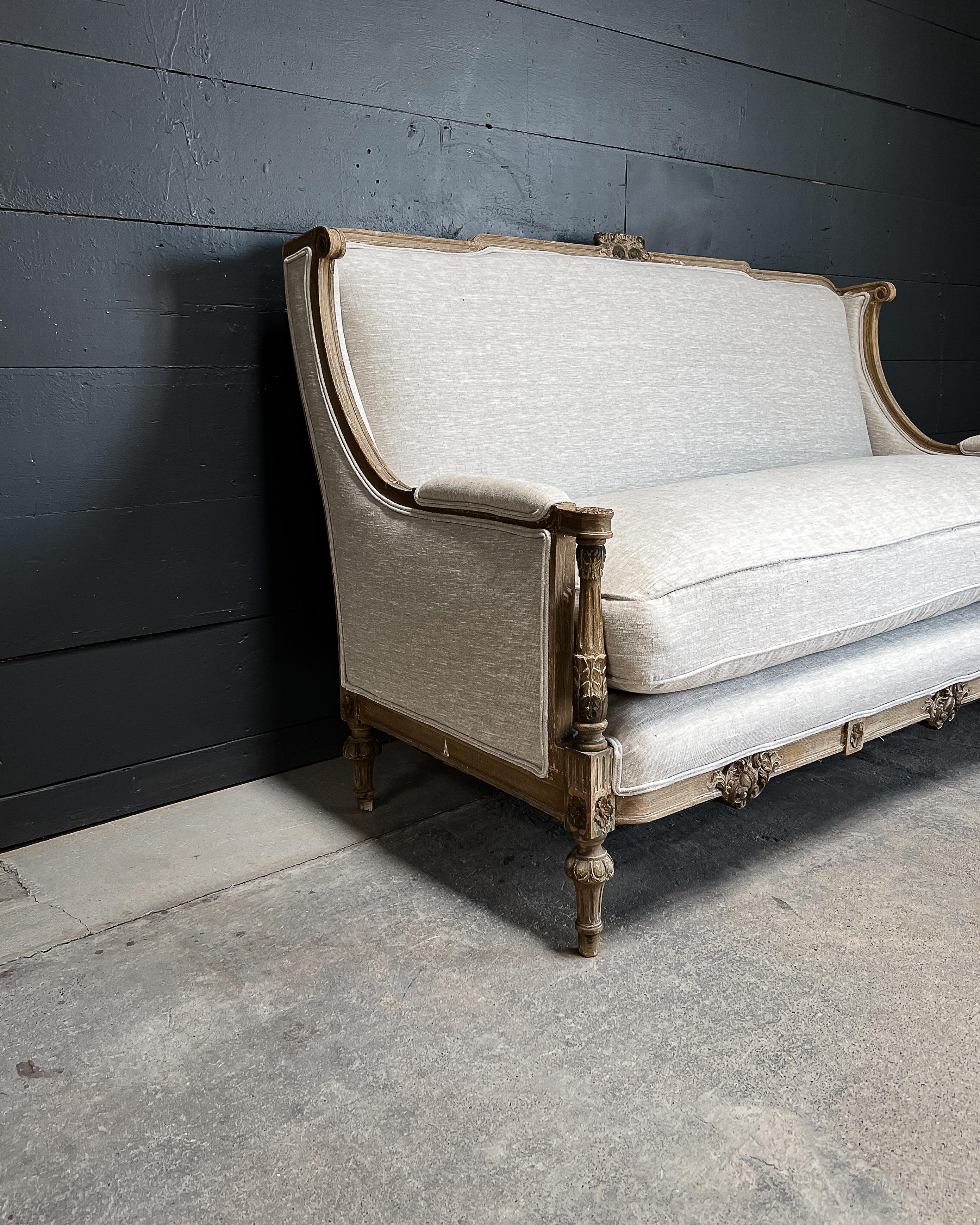 A stunning example of a Louis XVI style sofa with lovely hand-carved details including floral die joins, ornamental whorls, acanthus leaves and fluted legs. The frame features a beautiful distressed patina, while the (recently reupholstered) creamy