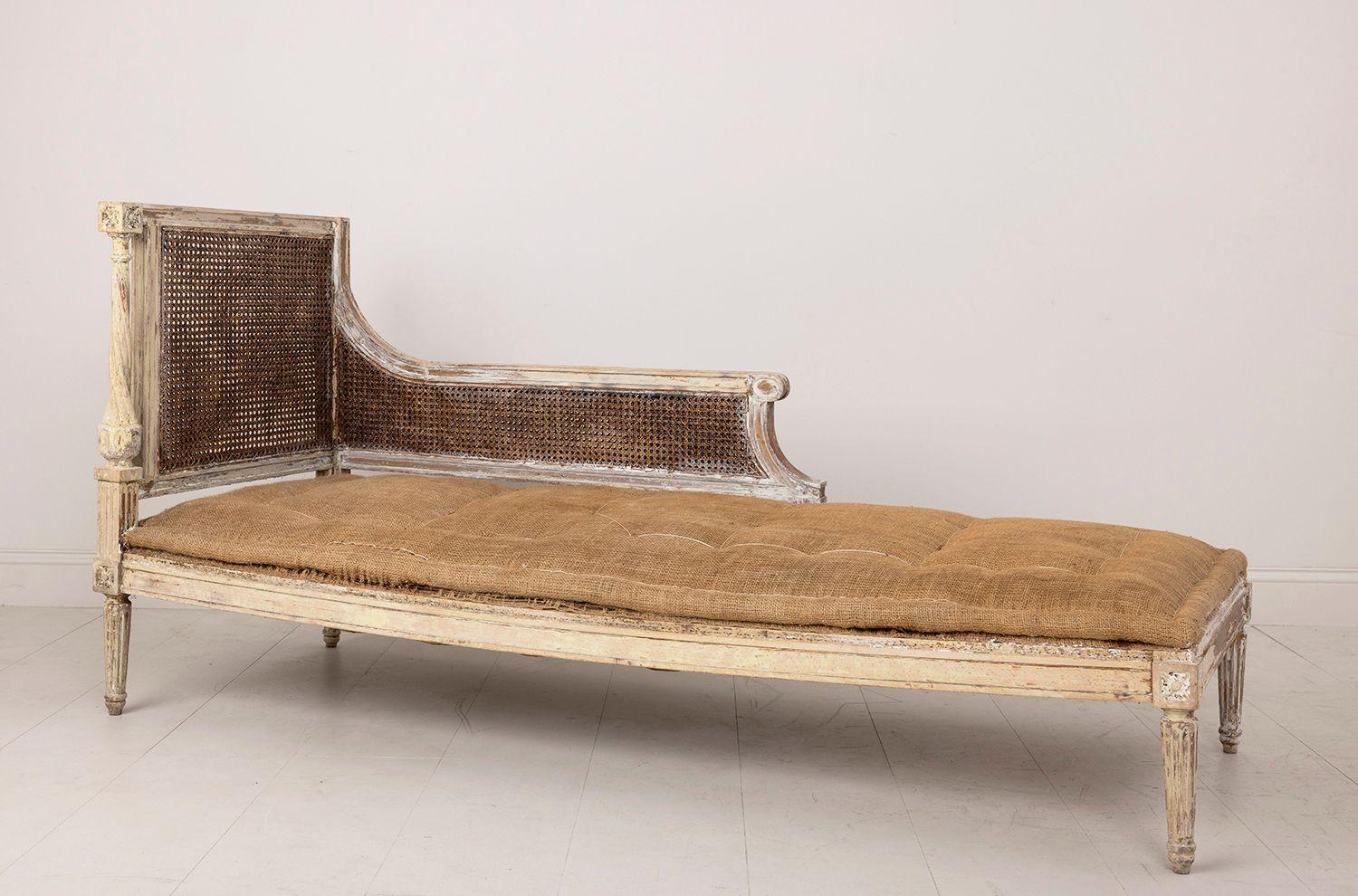 A 19th c. French chaise lounge or daybed in the Louis XVI style with original caned back and side. This piece is wearing old paint with traces of original gilt. The backside of the caning is painted. The seat material shown in the images has been