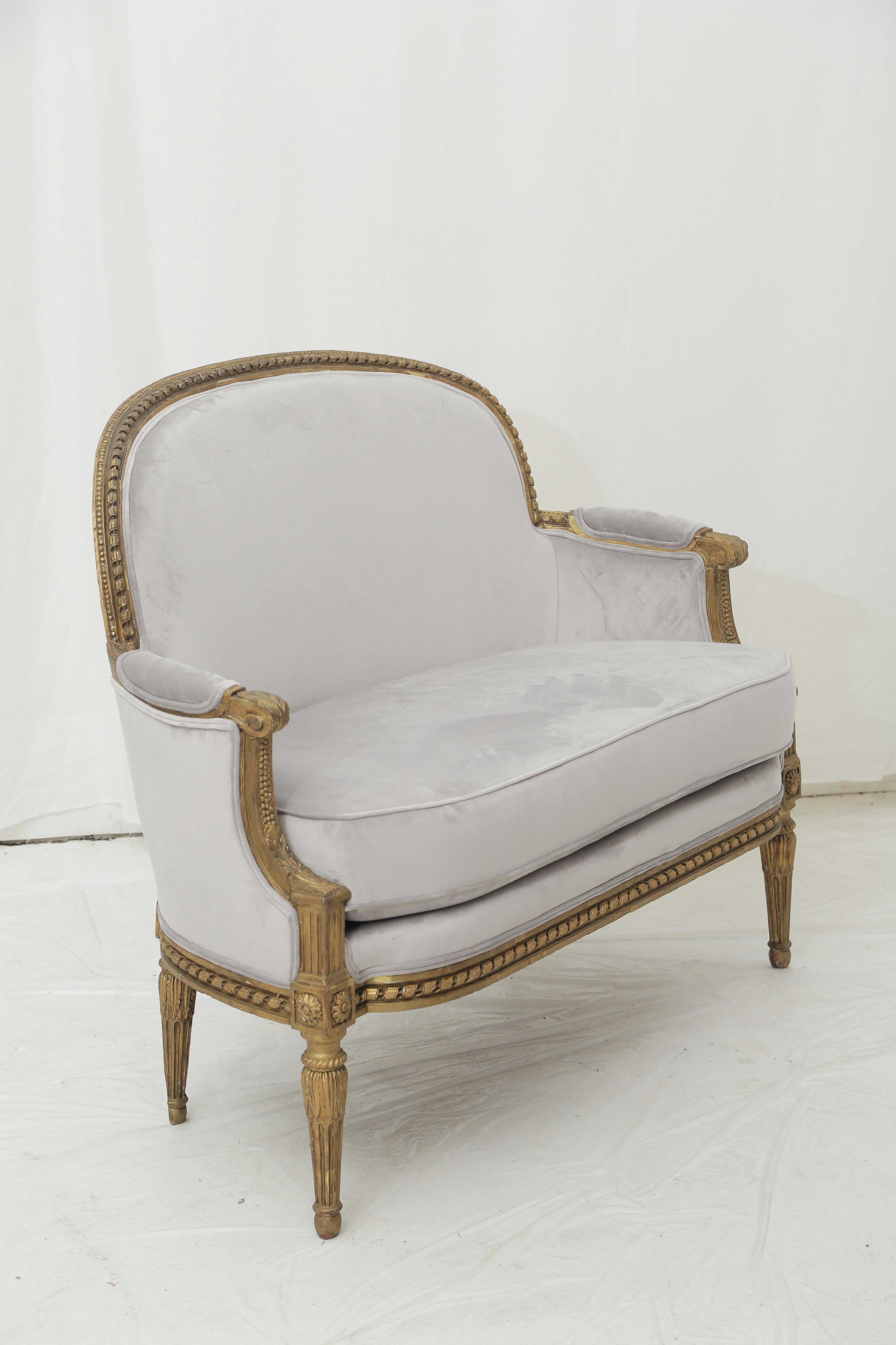 Recently refinished, this French loveseat is in the Louis XVI style. Carved giltwood and pale grey soft suede upholstery. From the end of the 19th century. Tight beech frame. Some slight gaps in the sculpture and the layer of gold on the back of the