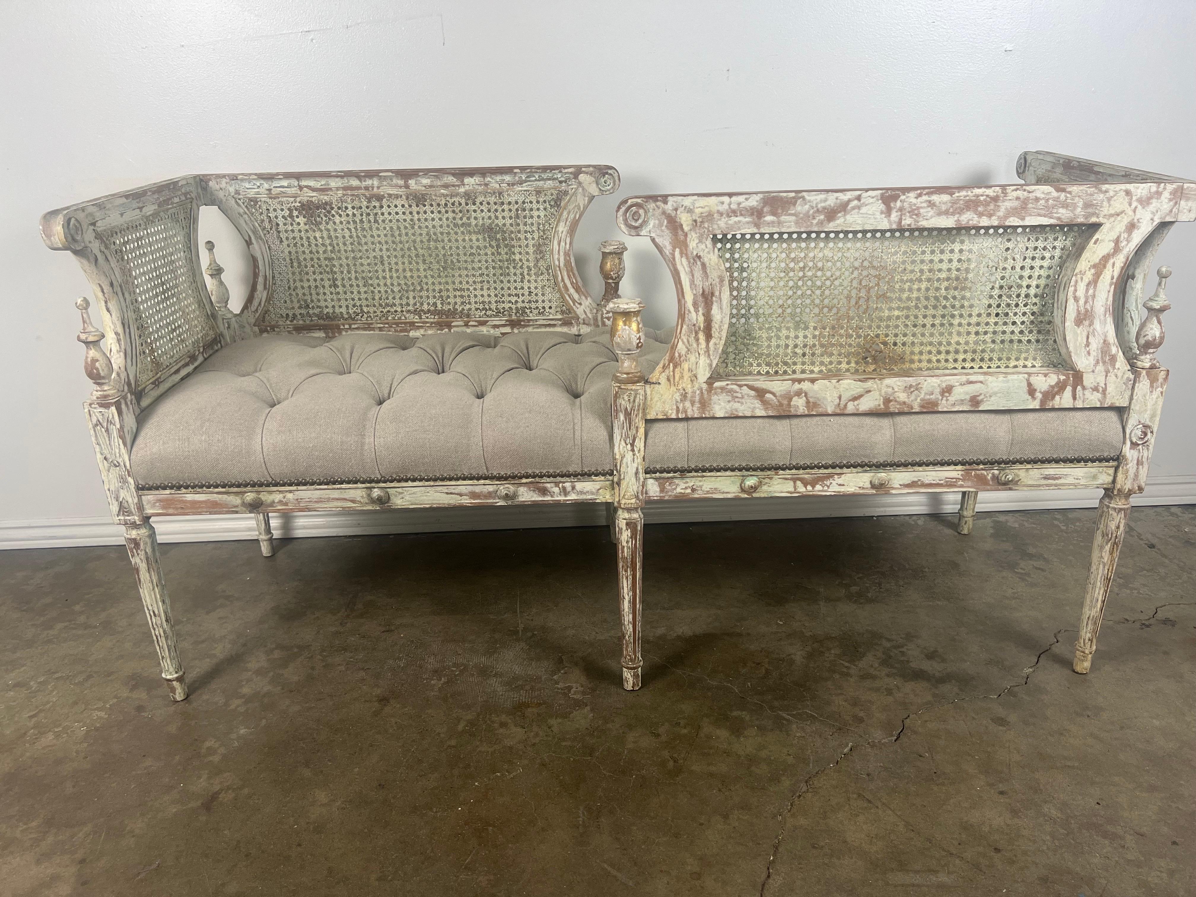 19th century Louis XVI style painted bench.  The bench has two seats that face in opposing direction.  This unique bench stands on six straight fluted legs.  The back and sides have the original cane.  The piece has a worn painted finish.  We