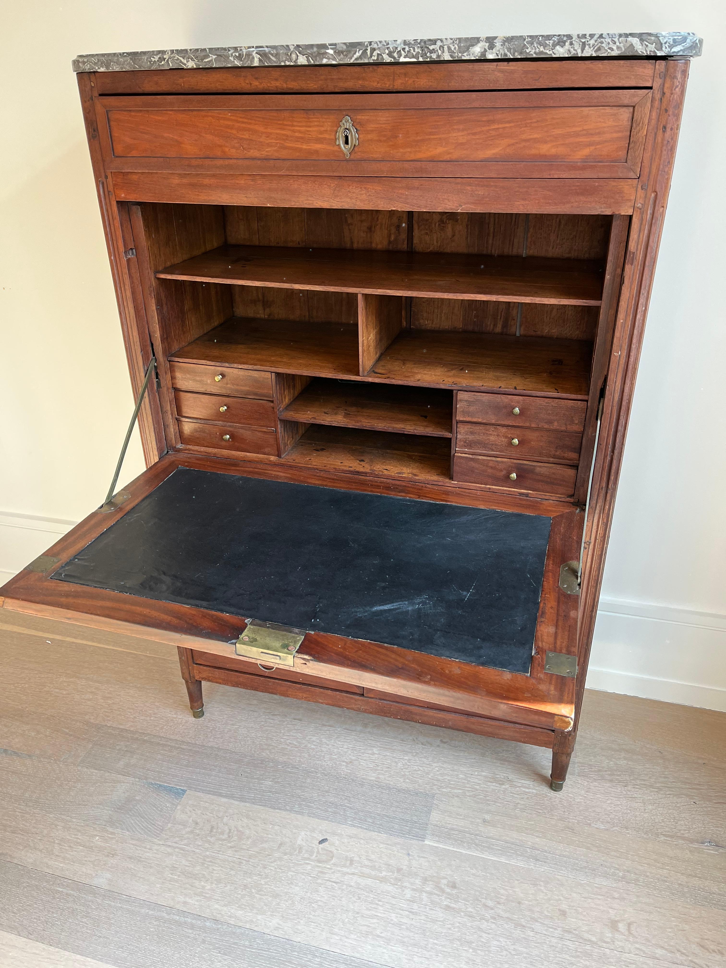 19th century French mahogany Secre´taire a` Abattant / fall-front desk with marble top. There is a single slim drawer at the top with a decorative escutcheon. The front of the desk folds down to reveal an interior outfitted with six smaller drawers,