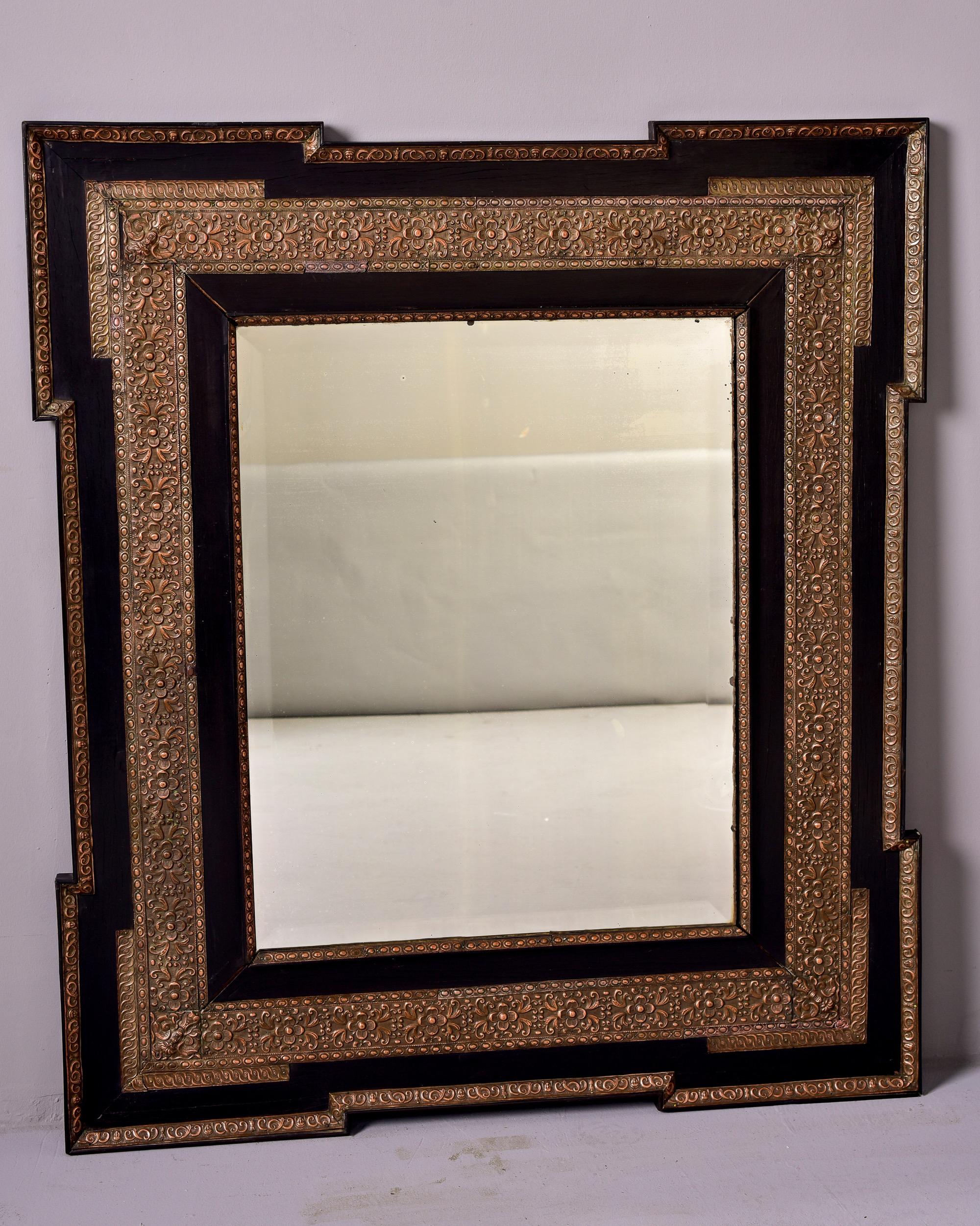 Circa 1880s French mirror with beveled edge in black frame with decorative pressed metal details on inner border and outer edge. Unknown maker.