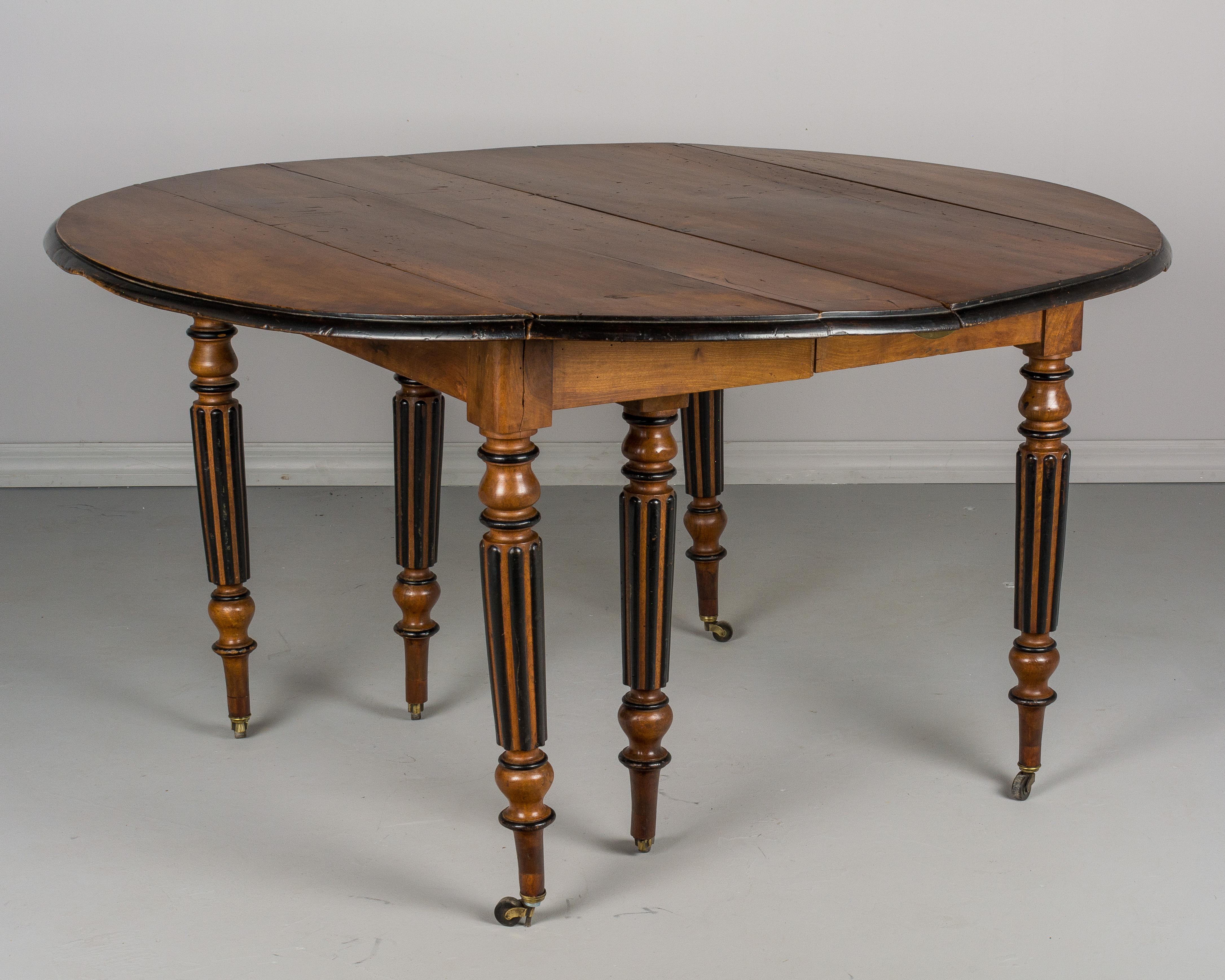 A 19th century French Napoleon III style drop leaf extension dining table made of solid walnut accented with black lacquer trim. Six fluted legs with brass castors. Table opens freely and has been raised to 29.5