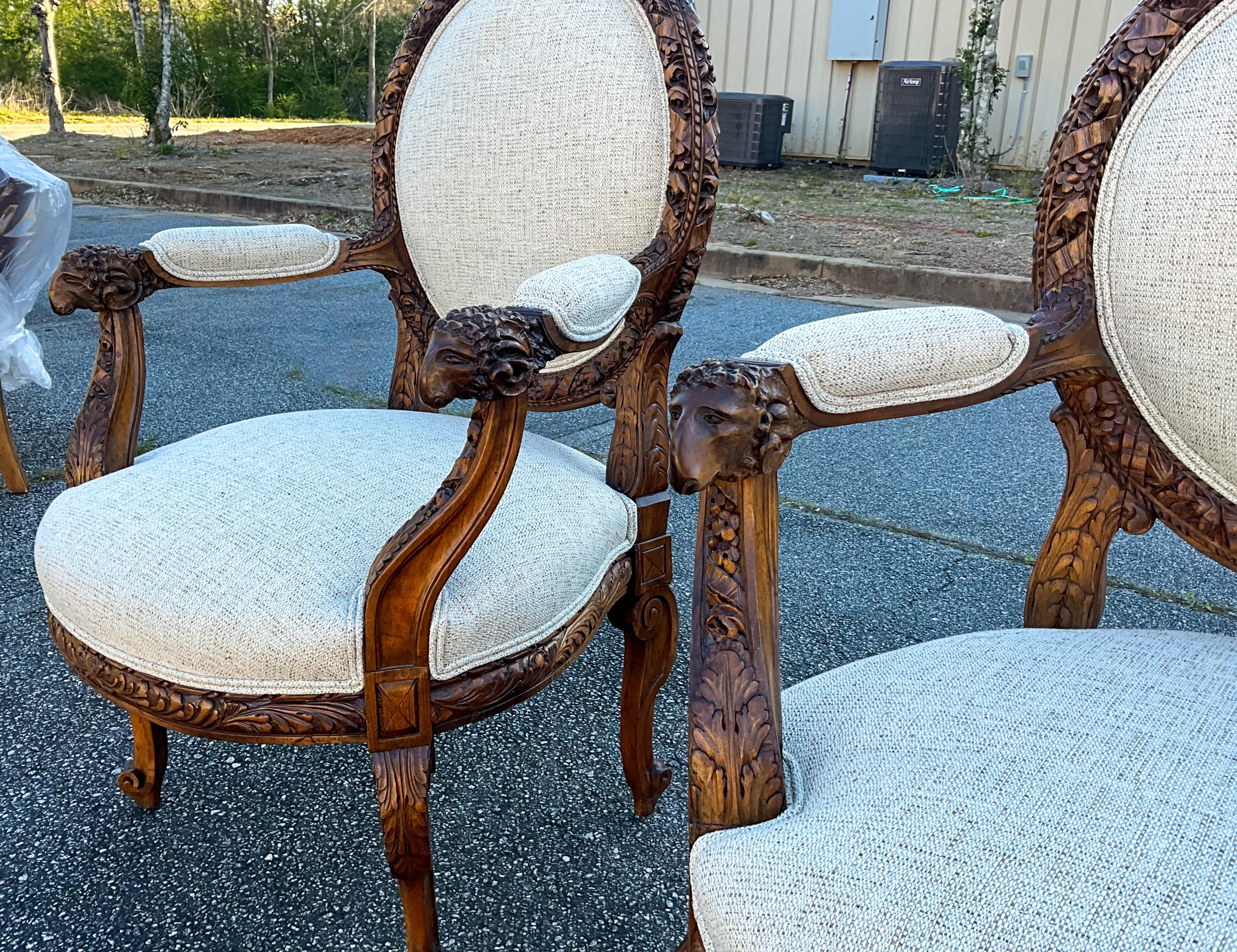 These are fabulous! This is a pair of heavily carved walnut French bergere chairs. They have Neo-classical styling with the ram form arms and instruments along the back frame. The linen blend fabric is new. The arms are 27” in height. 

My