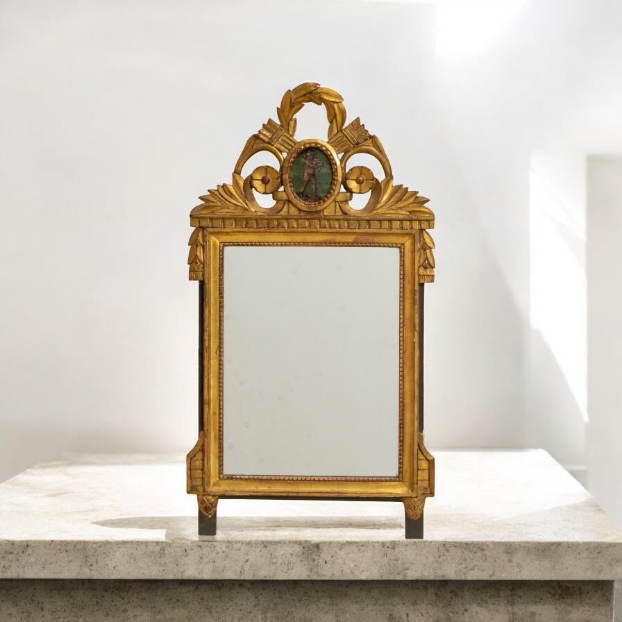 Se trata de un temprano espejo de pared francés de madera dorada tallada con estilo neoclásico de renacimiento. Observa el medallón de putti pintado a mano sobre fondo verde. El marco es dorado y de ébano y representa temas clásicos grecorromanos.