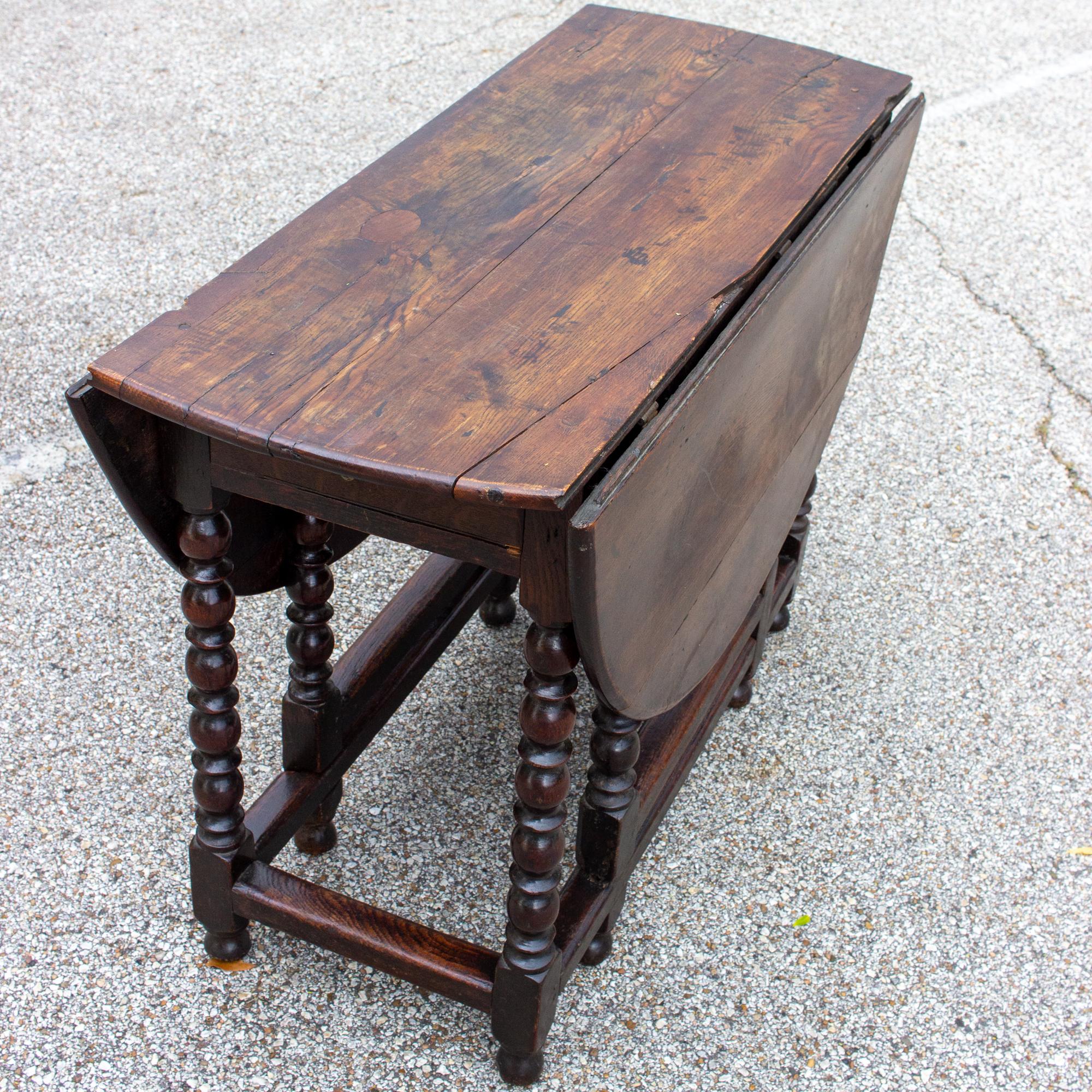 This antique French hand carved, oak gate-leg table features drop leaves on both sides, ball turned leg details and a center drawer for storage. The deep brown finish is likely original, and this piece can also be used as a console table when