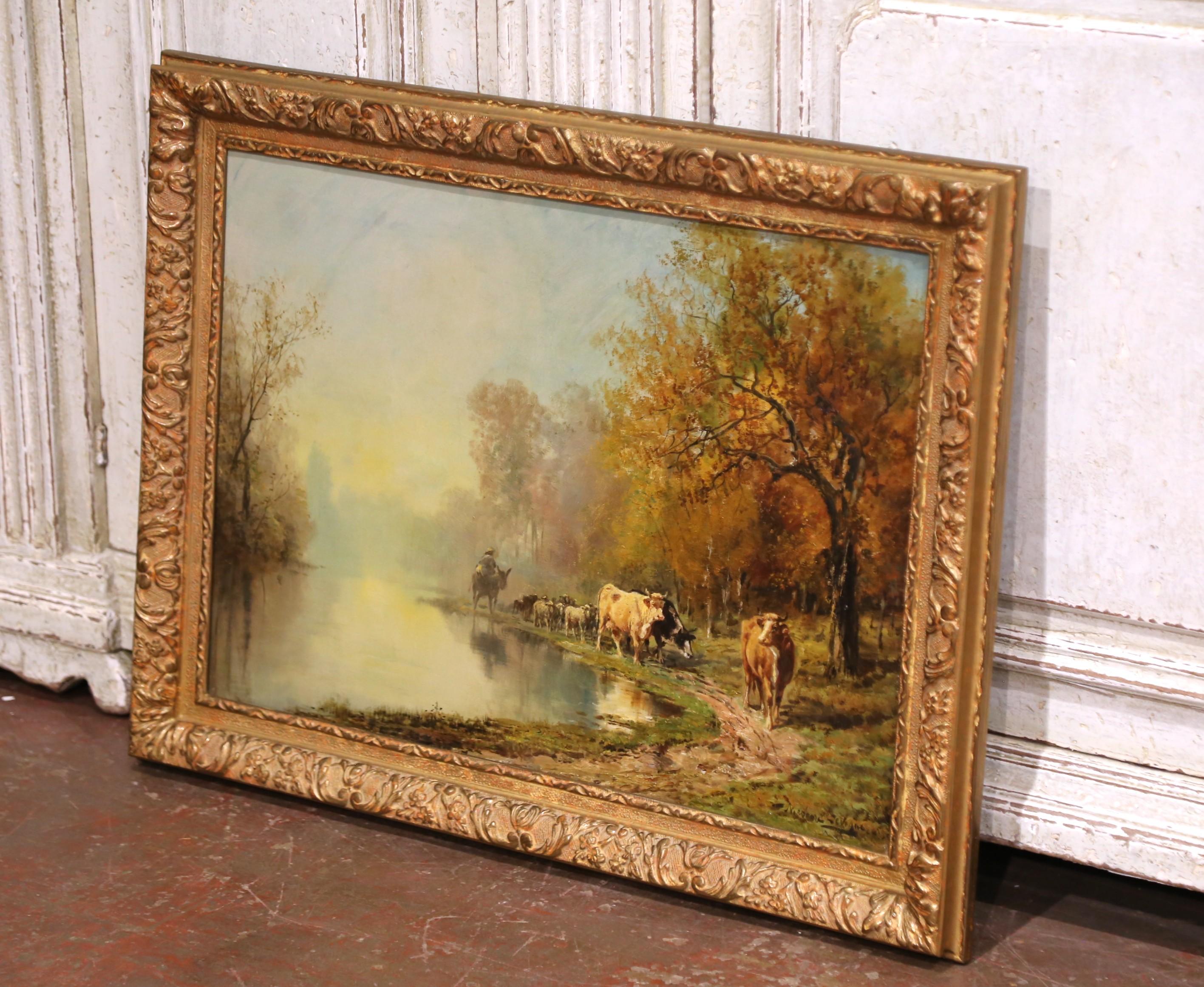 This antique oil on canvas painting by Théodore Levigne (1848–1912) captures a tranquil riverside scene at sunrise, as a herder leads cattle and sheep along a winding path beneath golden autumn trees. The reflective surface of the pond mirrors the