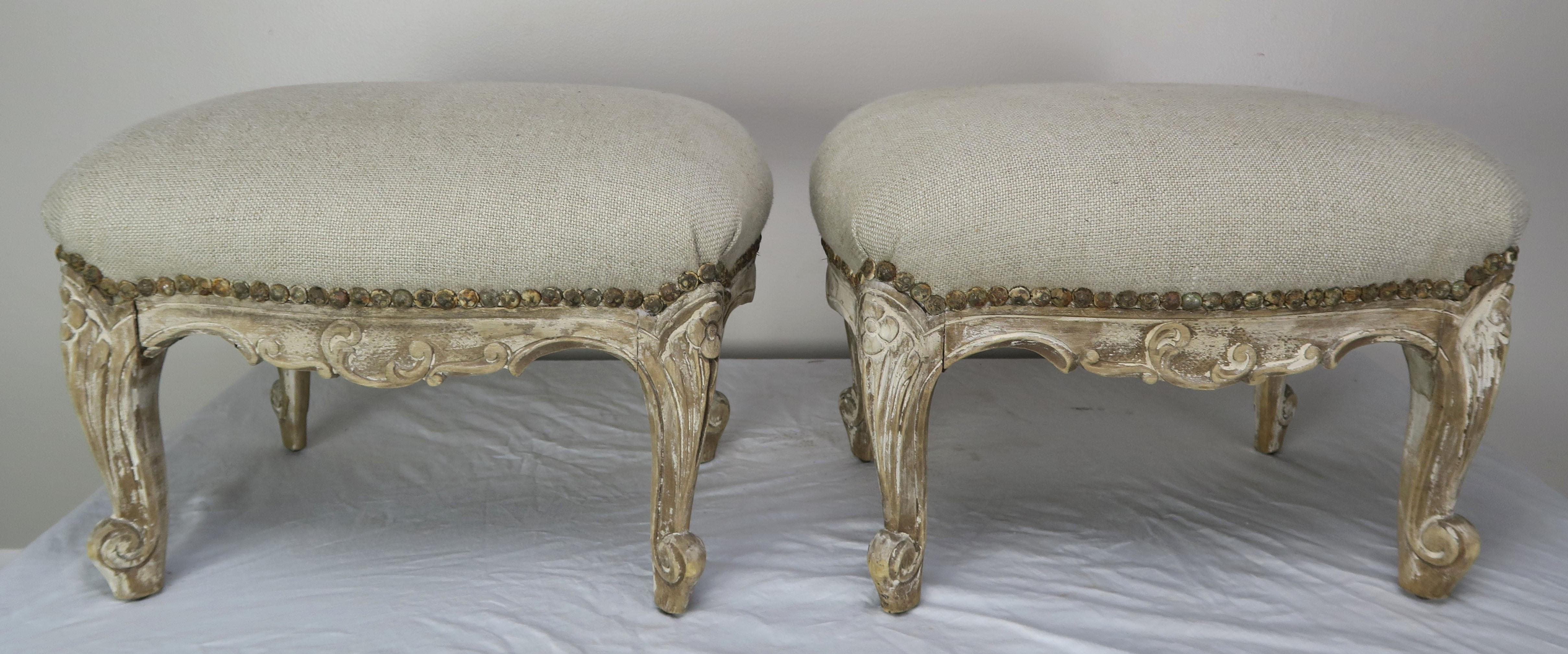 Pair of 19th century French Louis XV style painted benches or footstools. The benches stand on four cabriole legs that end in rams head feet. The painted finish is beautifully worn throughout. They are newly upholstered in washed Belgium linen with