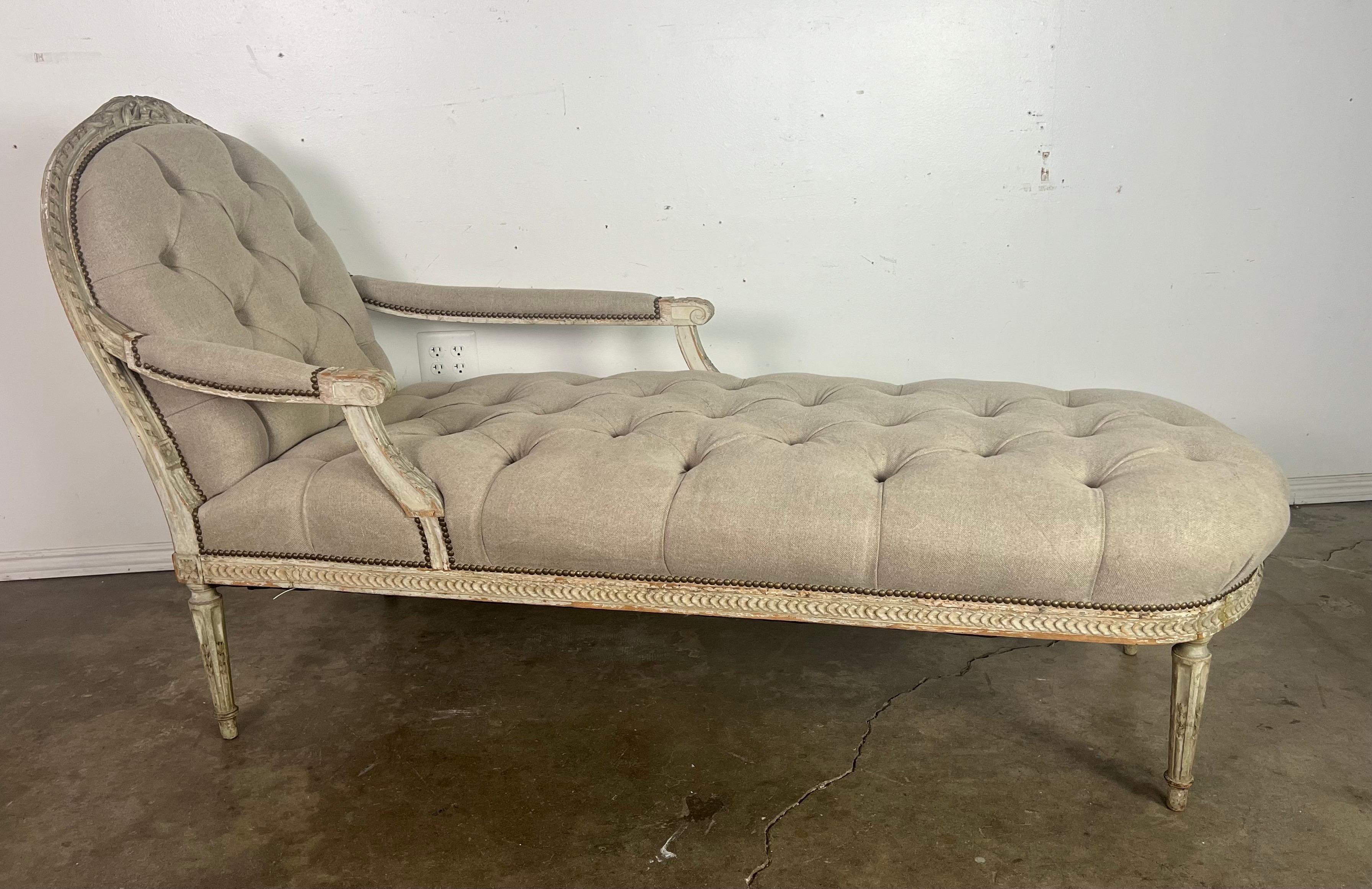 19th century painted chaise longue, characterized by its elegant and classic design.  The chaise is upholstered in a washed Belgium linen with tufting, creating a luxurious and textured look. The upholstery is finished with a row of nailheads.

The
