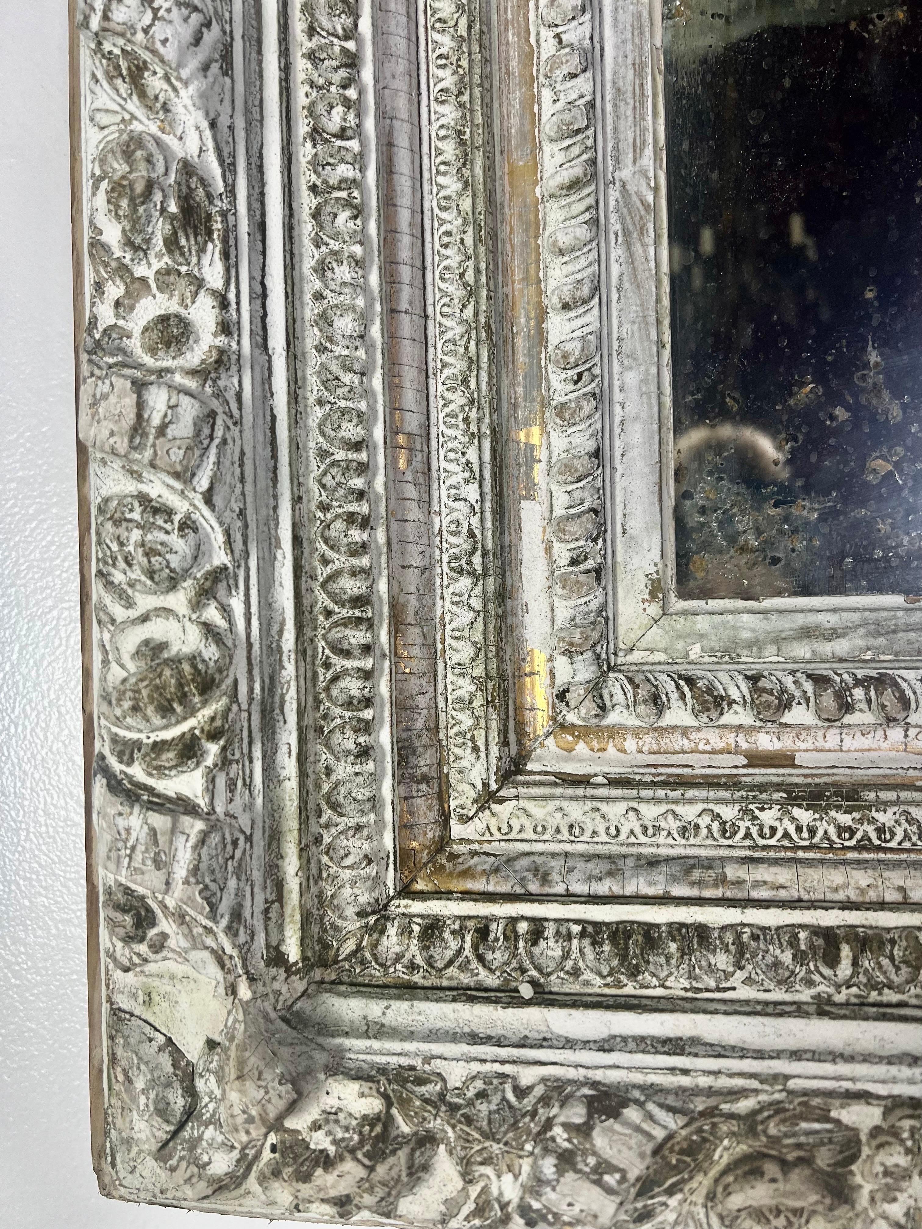 19th century carved wood & gesso mirror. There are remnants of a gold leaf finish from years ago, but the mirror is white/gray in color. The frame is adorned with finely carved details throughout. The finish is beautifully worn but there are bits of