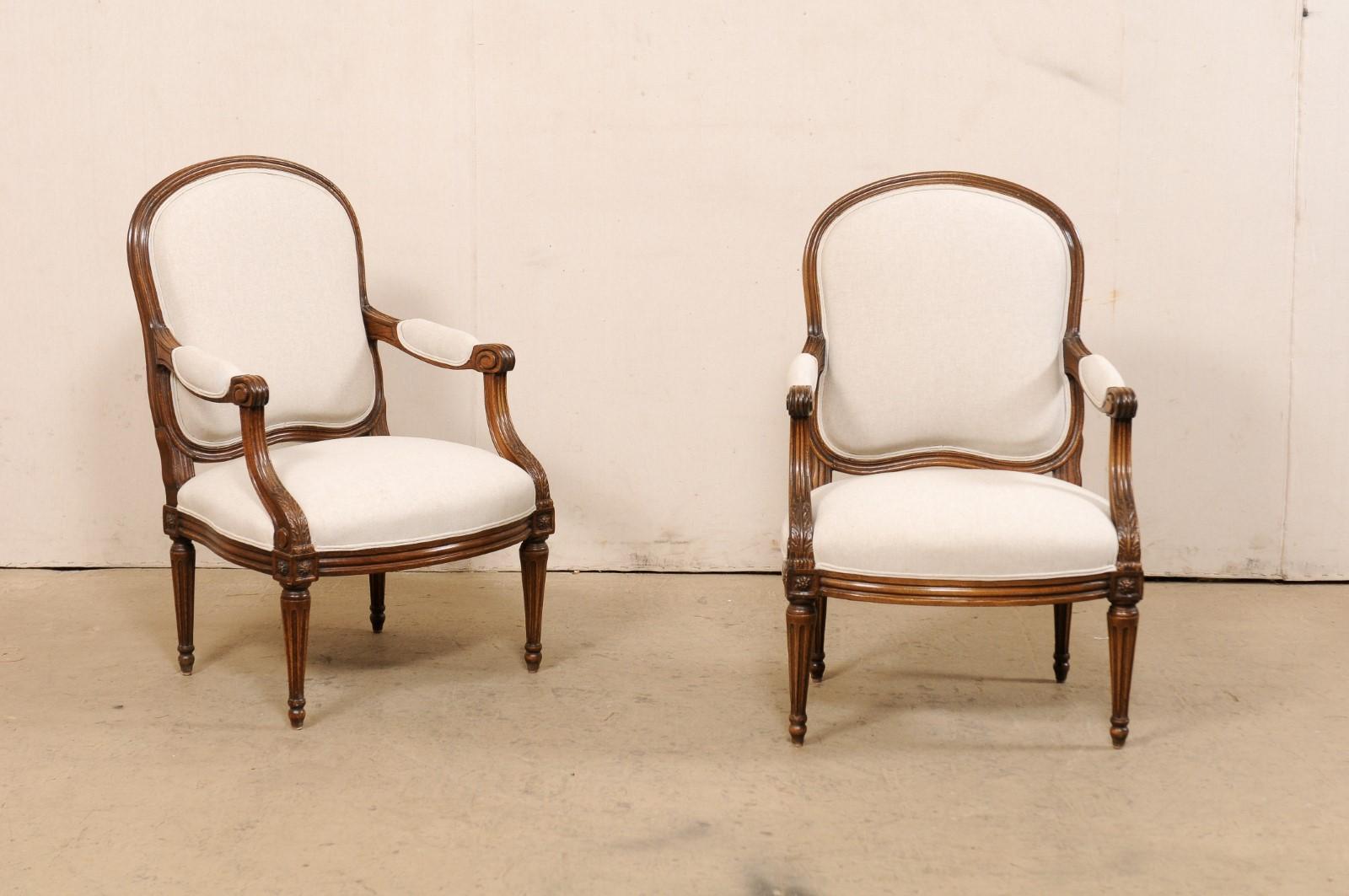 A French pair of timeless and elegant Louis XVI style armchairs from the 19th century. This antique pair of chairs from France each features a shapely, upholstered back, with elegantly arched crest rail, all framed within molded wood trim. Carved