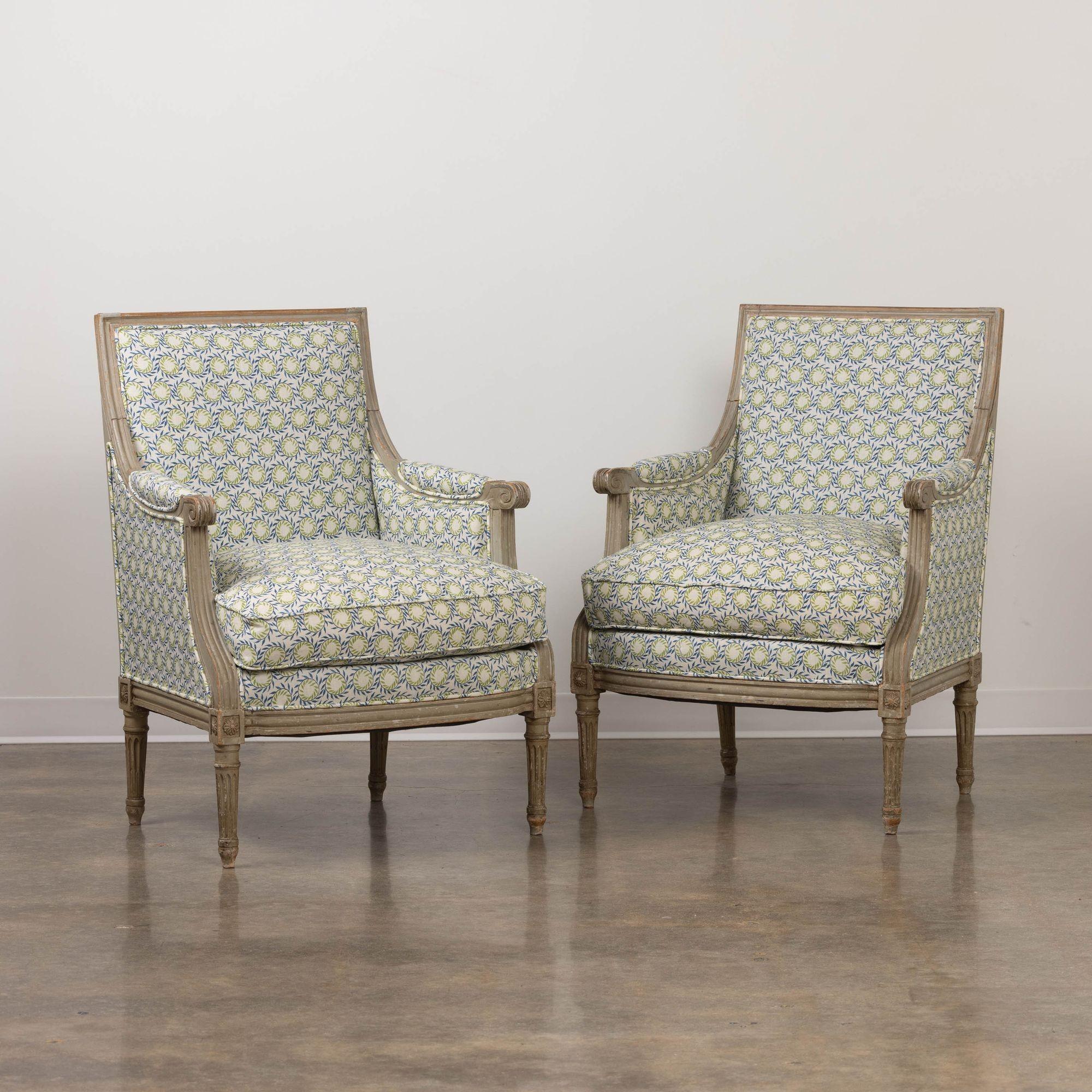 A pair of French Louis XVI style bergères in original paint from the 19th century. Rosettes on the corner posts with tapered and fluted legs. Newly upholstered in a smart blue and green fabric.  These beautiful chairs are very comfortable.