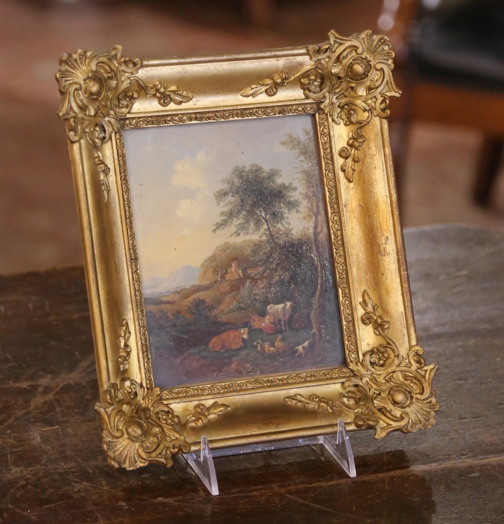 This charming 19th-century French landscape painting is executed on board and protected under glass within a finely cast giltwood frame. The pastoral scene features a tranquil grouping of livestock, cows, goats, sheep, and a herding dog, nestled