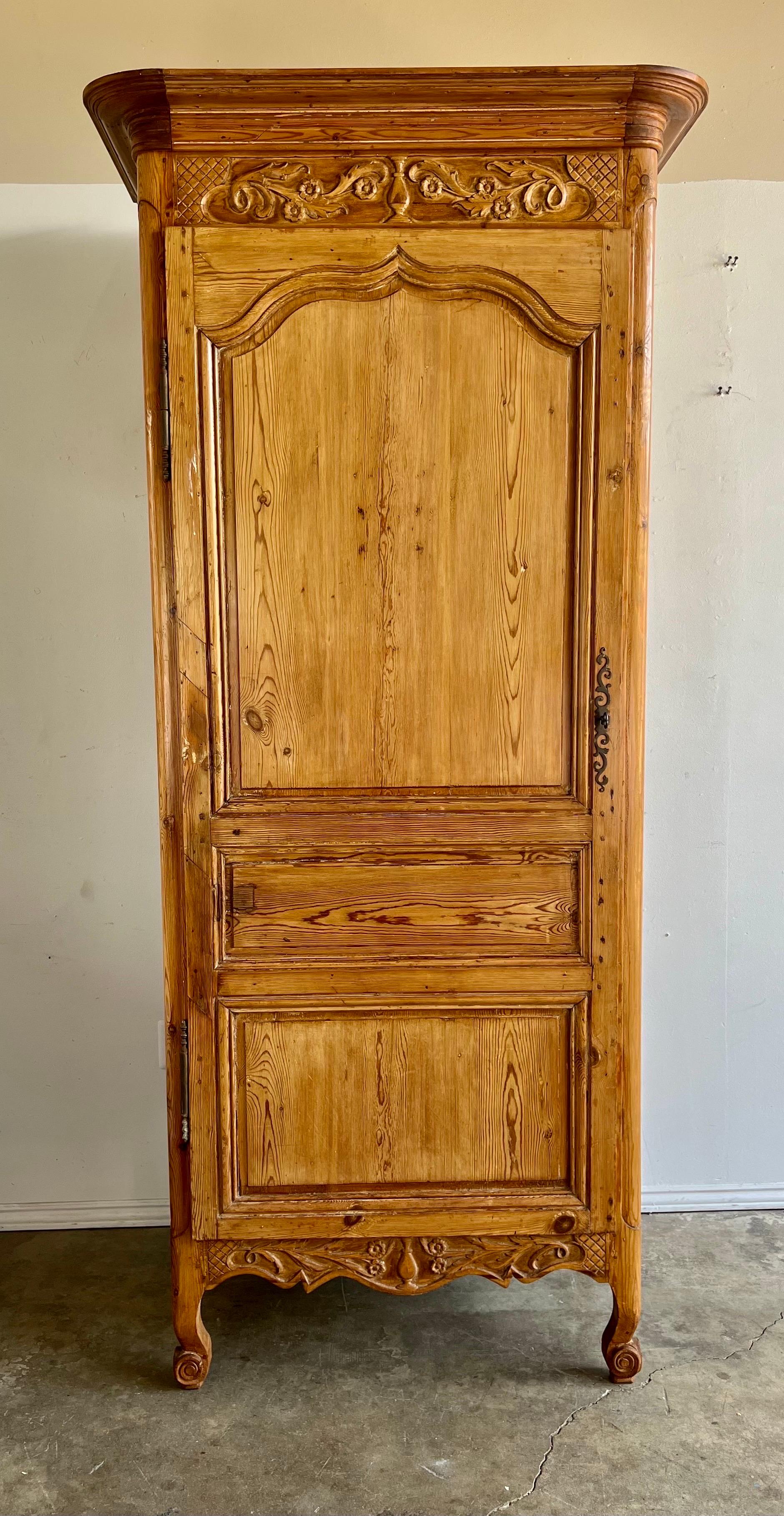 19th C. French Provincial style pine cabinet. There is one door that reveals great storage. The piece stands on four cabriole legs with rams head detail. Carving at top depicts swirling acanthus leaves and flowers flanking a center urn.