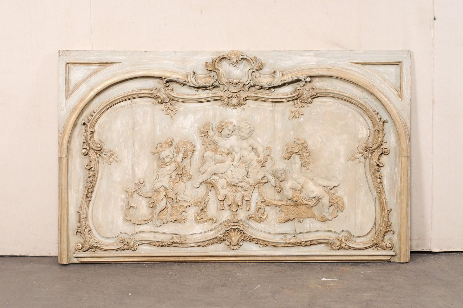 A large-sized French relief-carved and painted decorative wall panel from the 19th century. This antique plaque from France is rectangular-shaped with beautiful relief carvings depicting various putti at play alongside a monkey with tambourine and