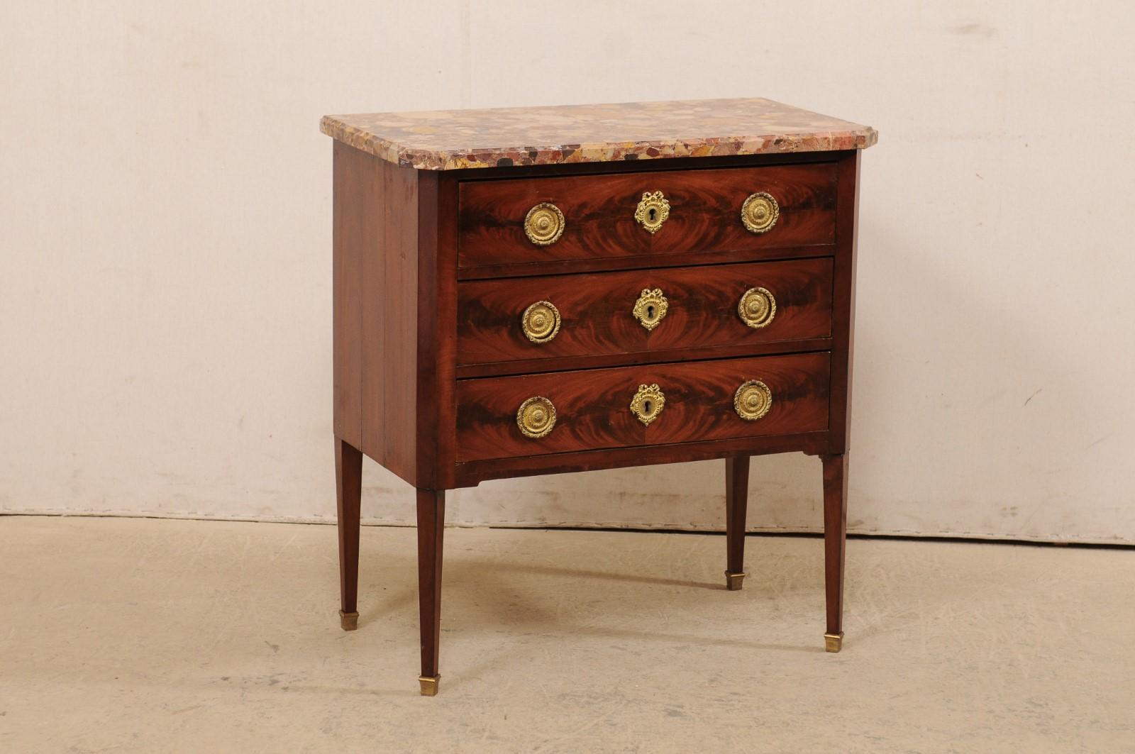 A French commode on legs with stone top and brass accents from the 19th century. This antique chest from France features a stone, likely scagliola, top with rounded, coved-edging and accentuated both front corners, atop a case with canted side posts