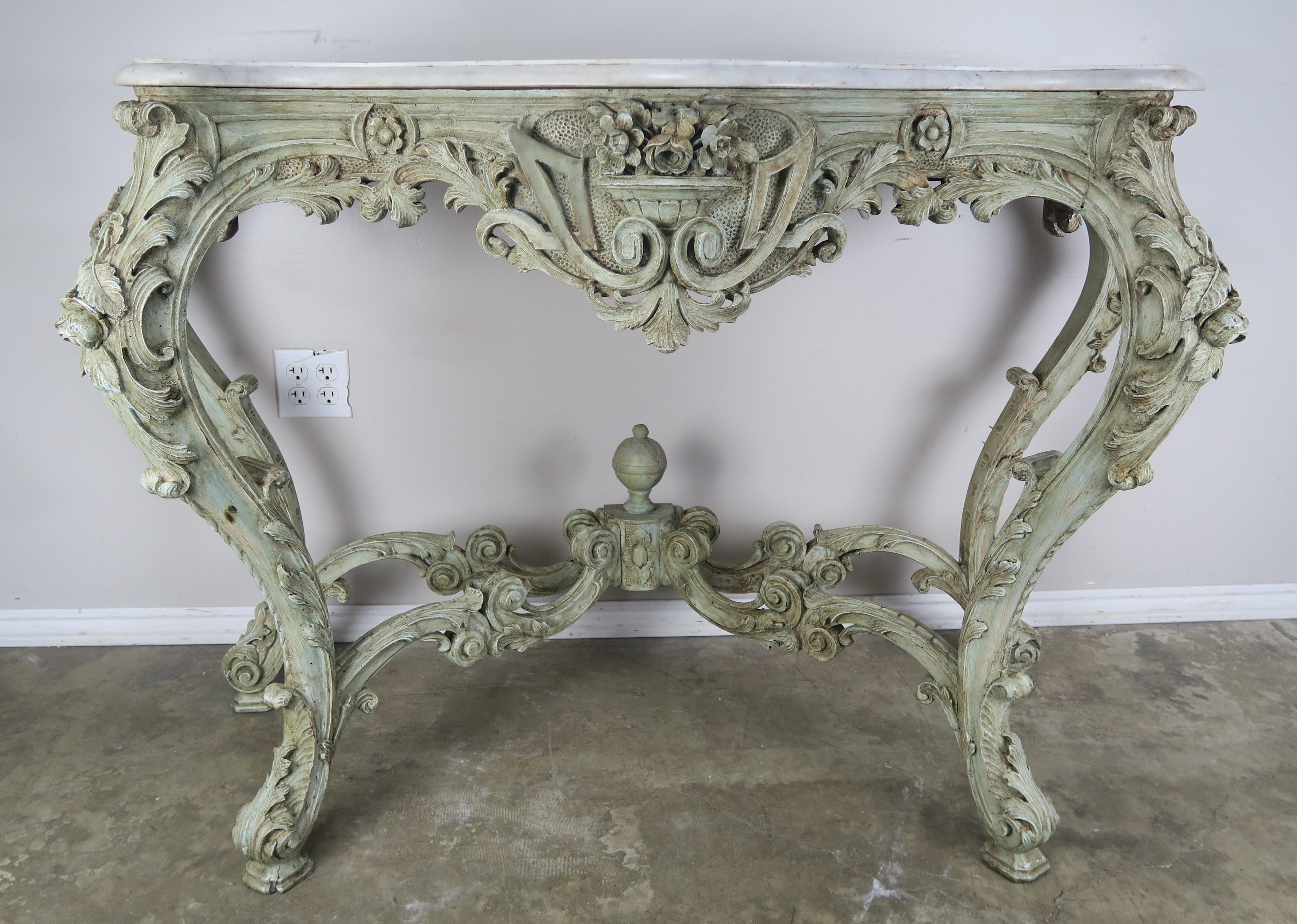 19th century French Rococo style painted console with Carrara marble top. The console is ornately carved with a center flower urn and scrolled acanthus leaves carved throughout. The console is painted in a soft green celadon coloration. The table