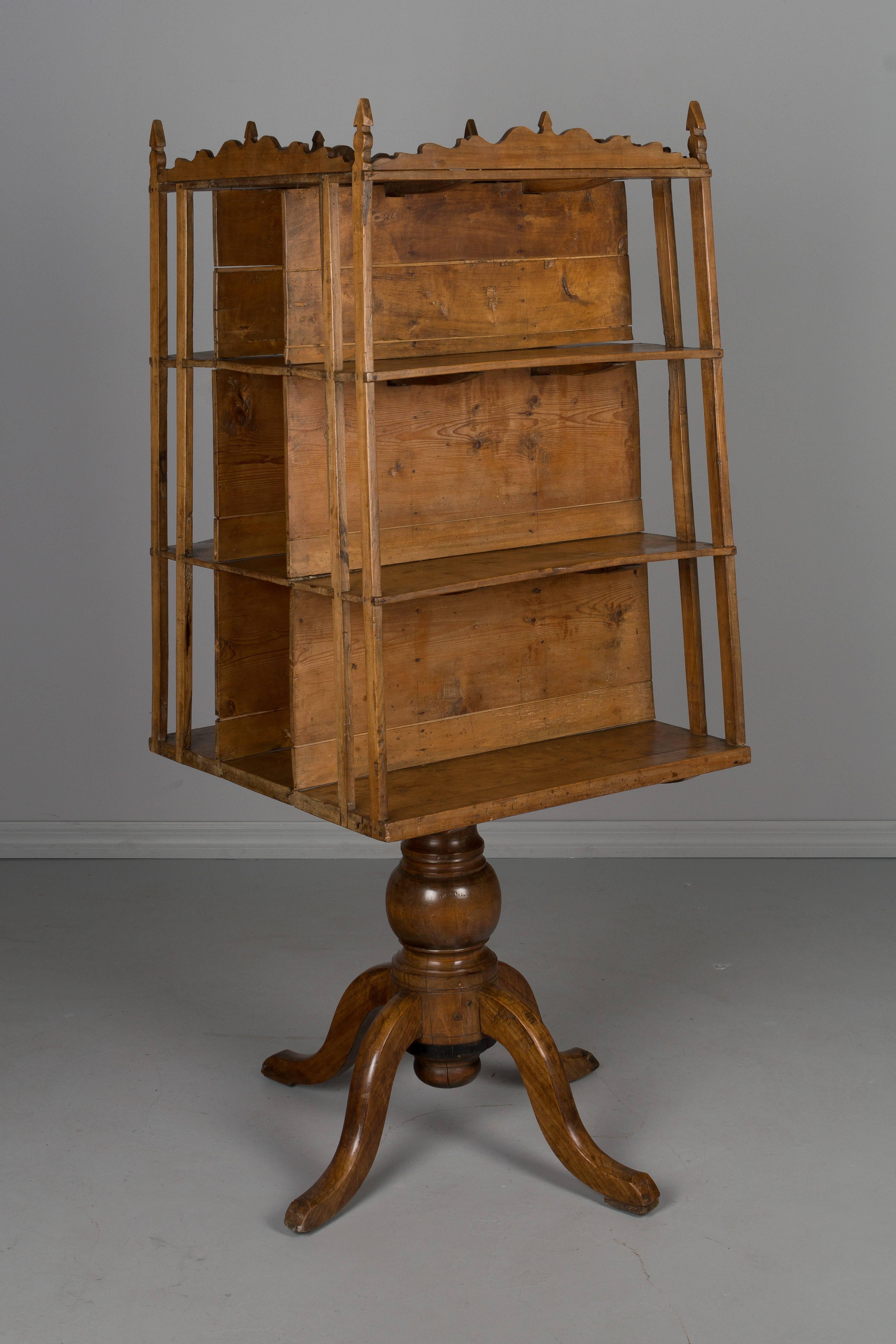 A 19th century French rustic rotating bookshelf made of cherrywood. In two parts, the book shelf has a hole through the middle and fits onto the post of the heavy turned pedestal base. Simple decorative trim at the top. This was used as a store