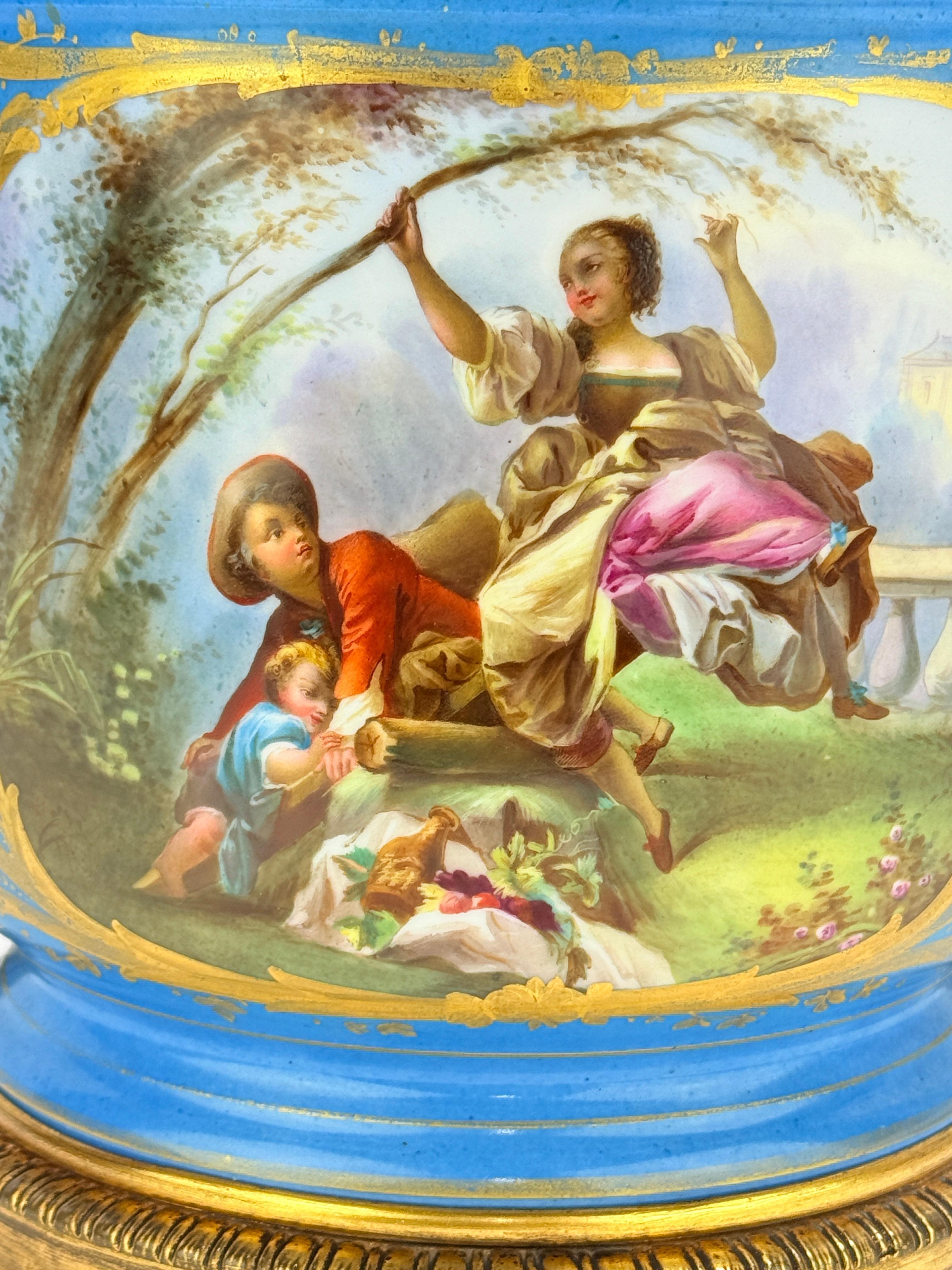 Un cachepot in porcellana francese riccamente decorato nello stile di Sèvres, risalente alla fine del XIX secolo e montato in bronzo dorato finemente cesellato. Un lato presenta una scena di festa galante rococò alla Boucher o alla Fragonard, con