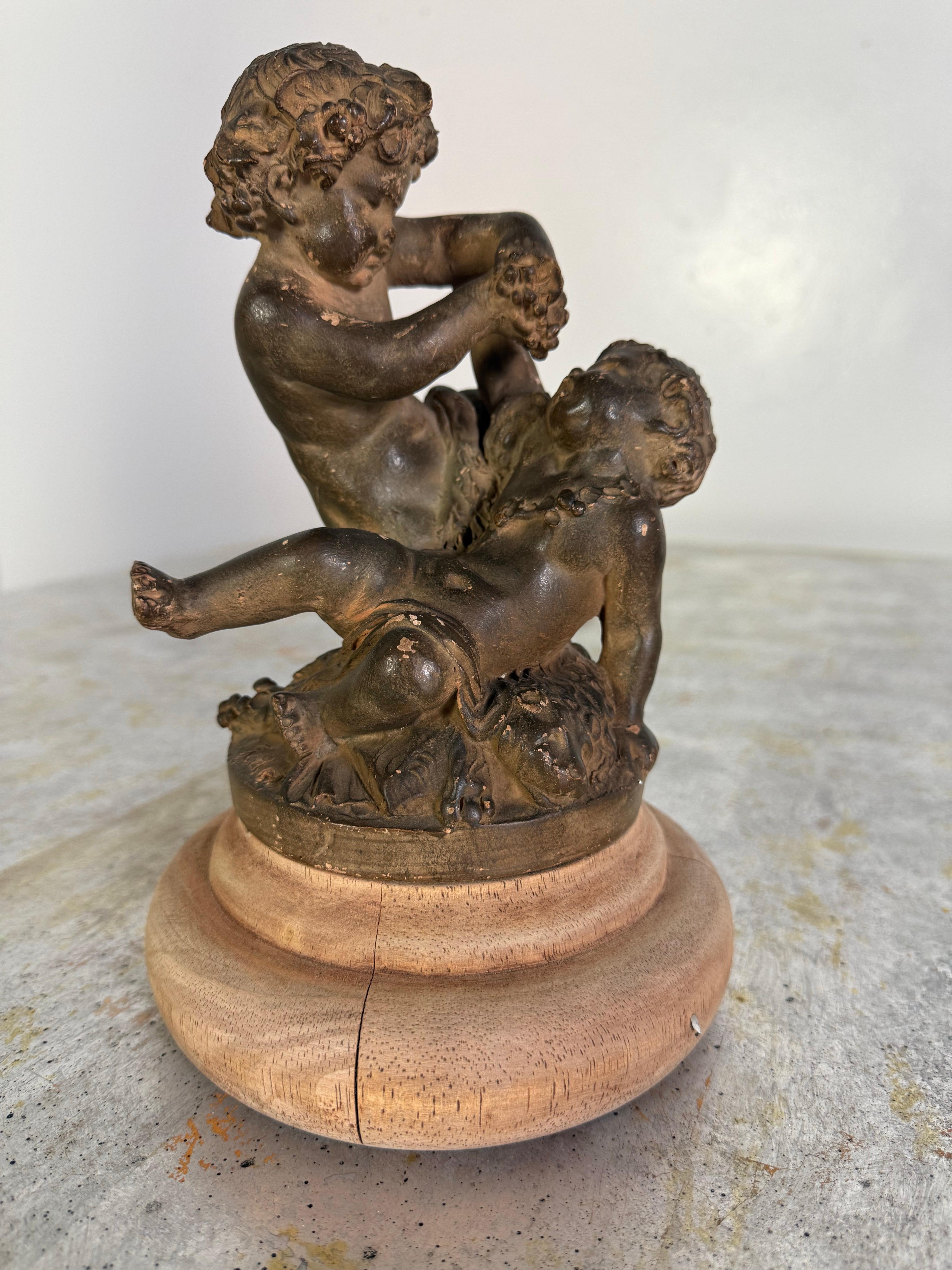 Cette charmante sculpture française en terre cuite du XIXe siècle représente deux putti enjoués dans une pose pleine d'entrain, représentant probablement des thèmes allégoriques ou pastoraux communs à l'époque. Les personnages sont rendus avec des