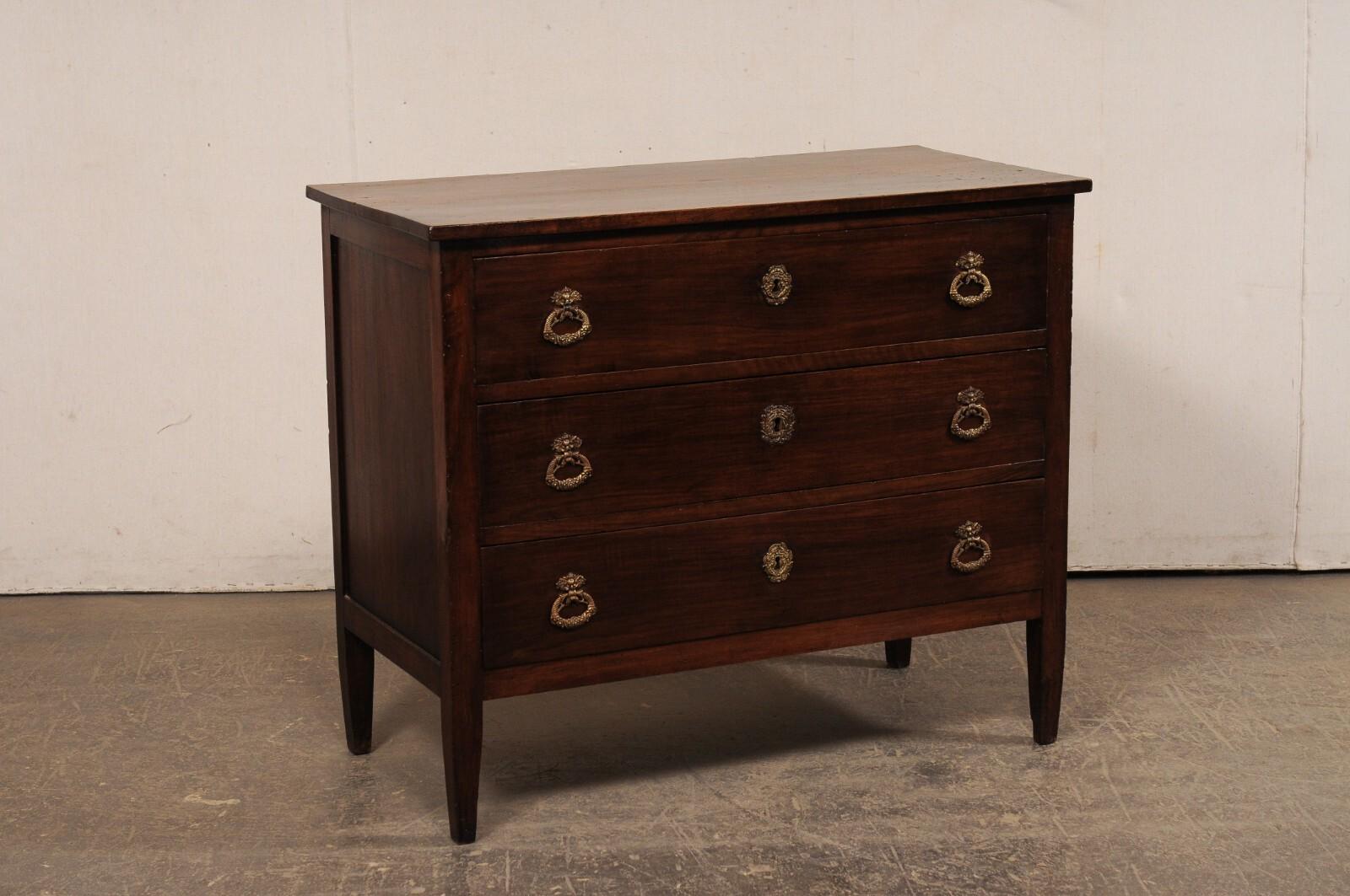 A French cleanly-designed, rich walnut wood, chest of drawers from the 19th century. This antique wooden commode from France features a rectangular-shaped top, above a case which houses three full-sized, dove-tailed drawers, and raised upon squared
