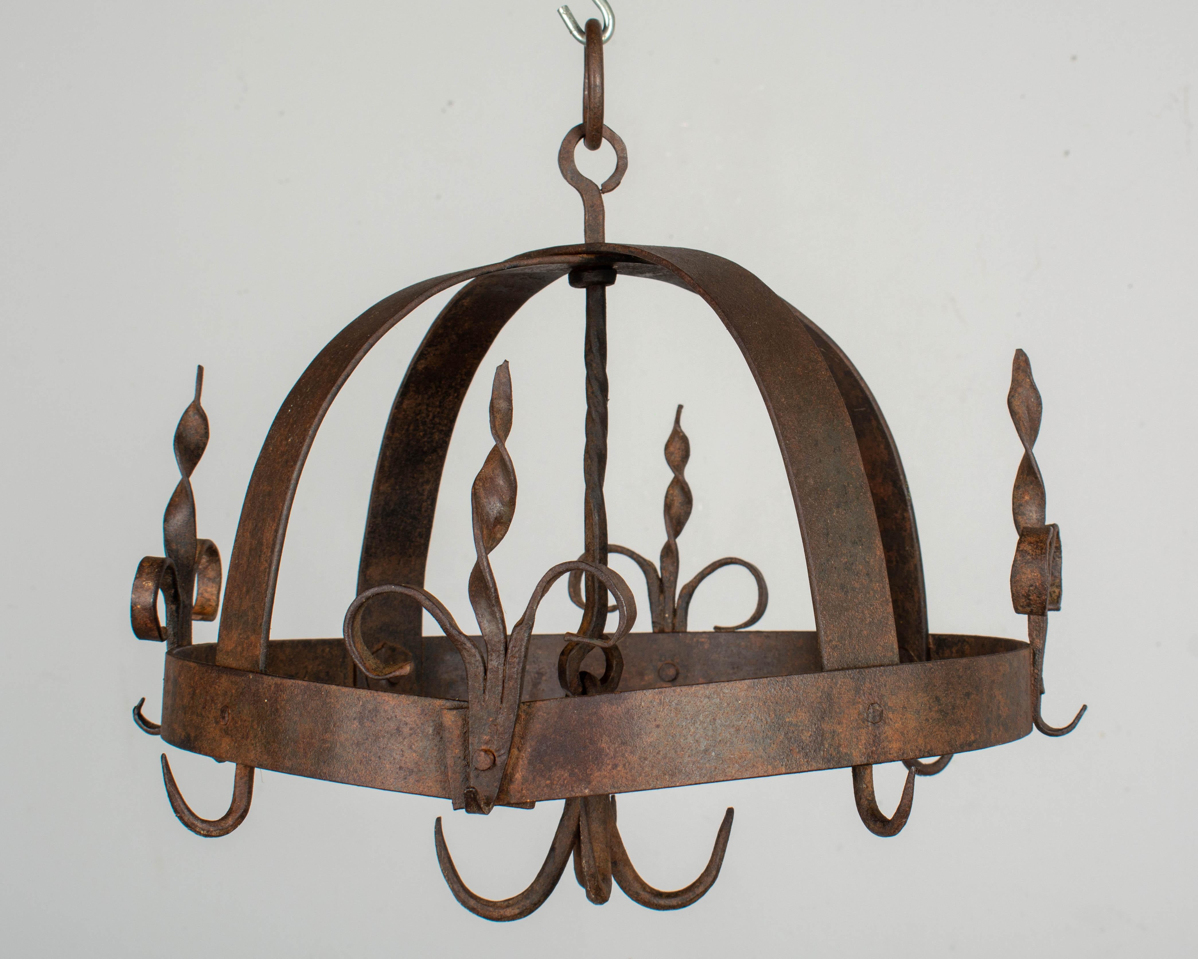 A rustic 19th century French wrought iron hanging pot rack with riveted construction. Four fleur de lis form decorative hooks around the perimeter and a cluster of four hooks dropping from the center.