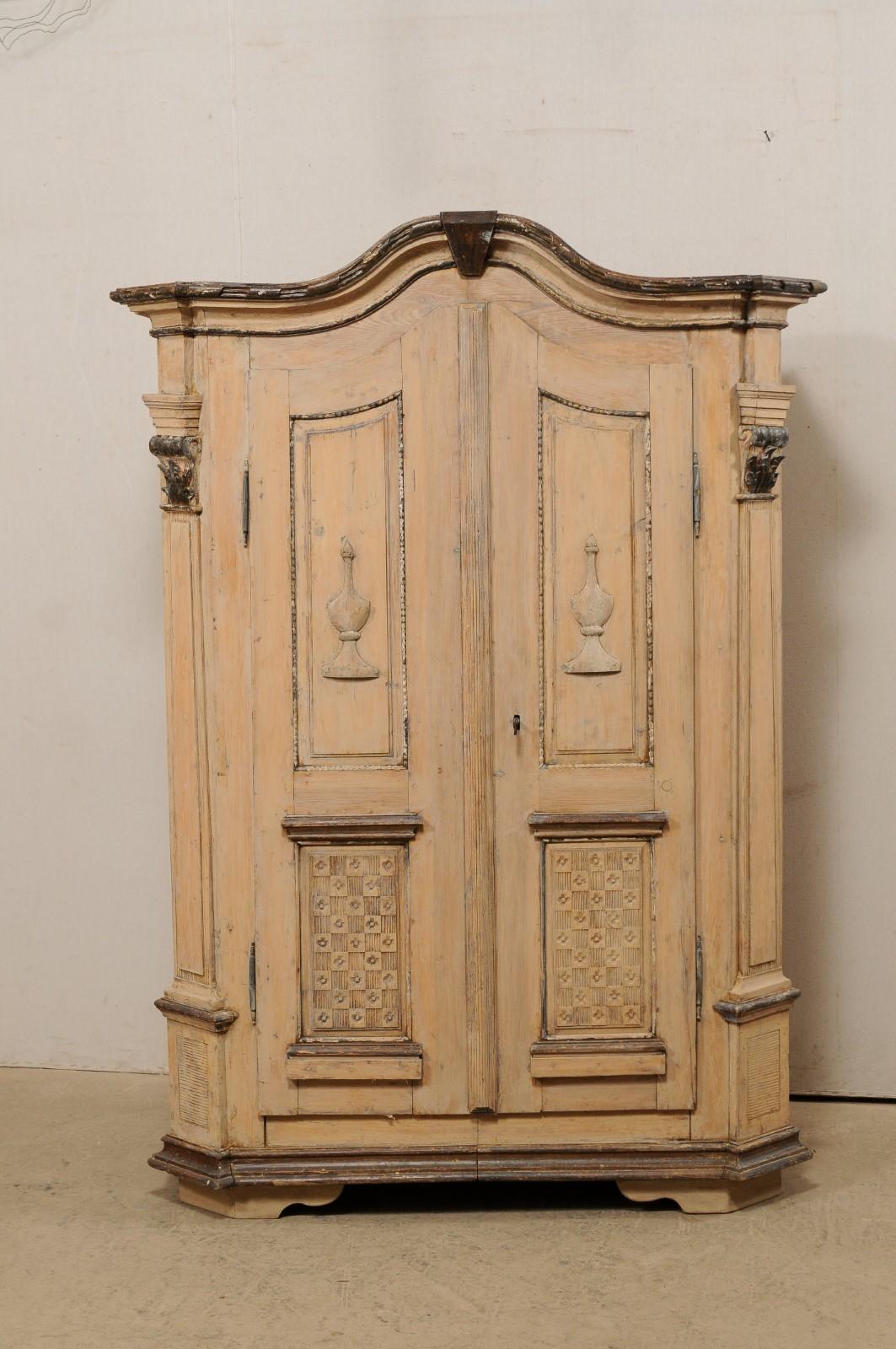 A German tall storage cabinet with nicely carved accents from the 19th century. This tall antique armoire cabinet from Germany features a molded and arched cornice, with carved ribbon trimming, atop a case which houses a pair of decoratively paneled