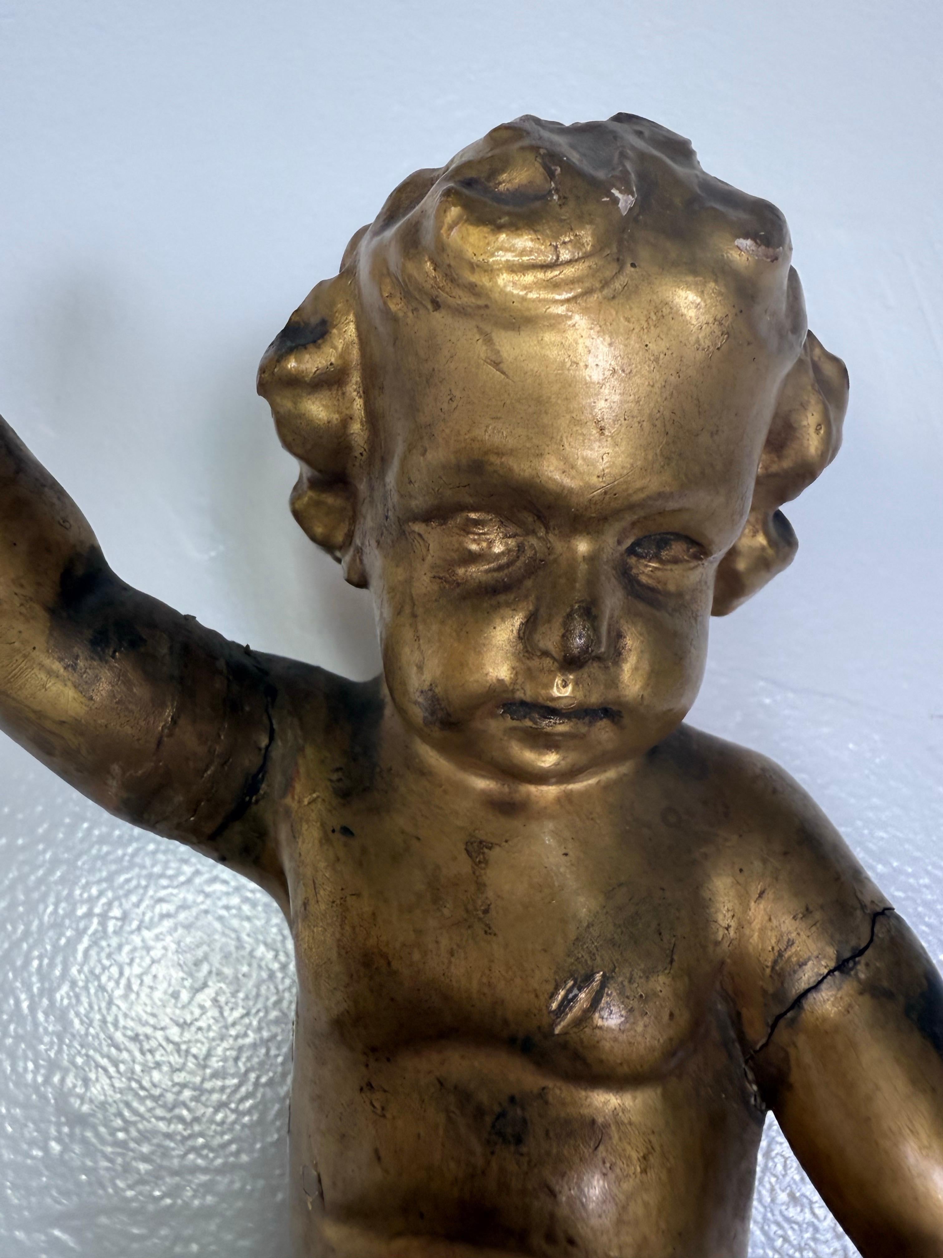 A beautifully detailed 19th century Italian giltwood architectural fragment featuring a seated cherub atop an ornate classical base. The finely carved putto is depicted with one arm raised in a playful gesture, perched on a pedestal adorned with a