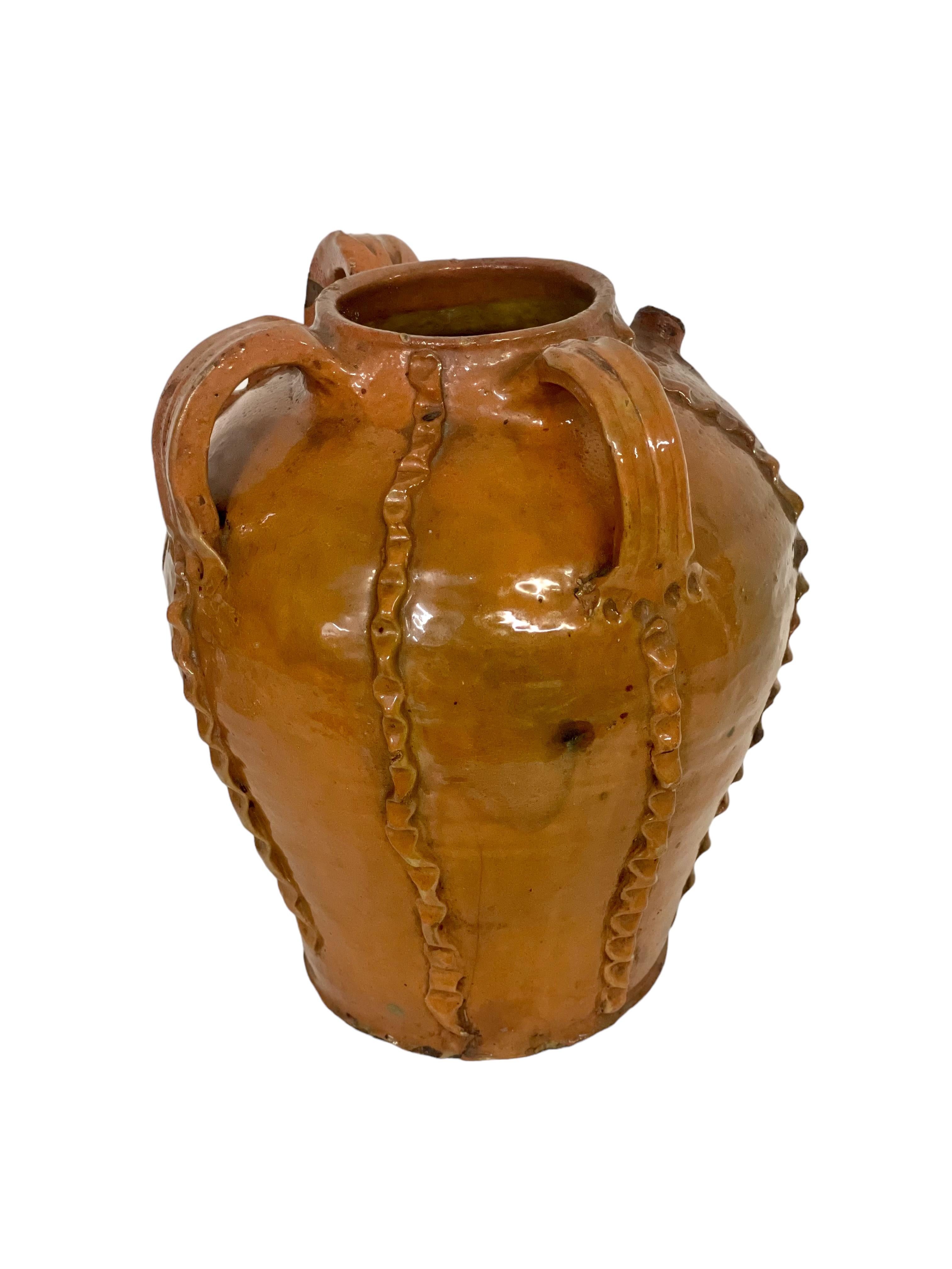 Ein hoher und formschöner antiker Ölkrug aus Nussbaumholz, der aus der Dordogne-Region in Frankreich stammt. Er ist vollständig in einem satten und glänzenden Goldbraun glasiert und zusätzlich mit mehreren applizierten und gekniffenen vertikalen