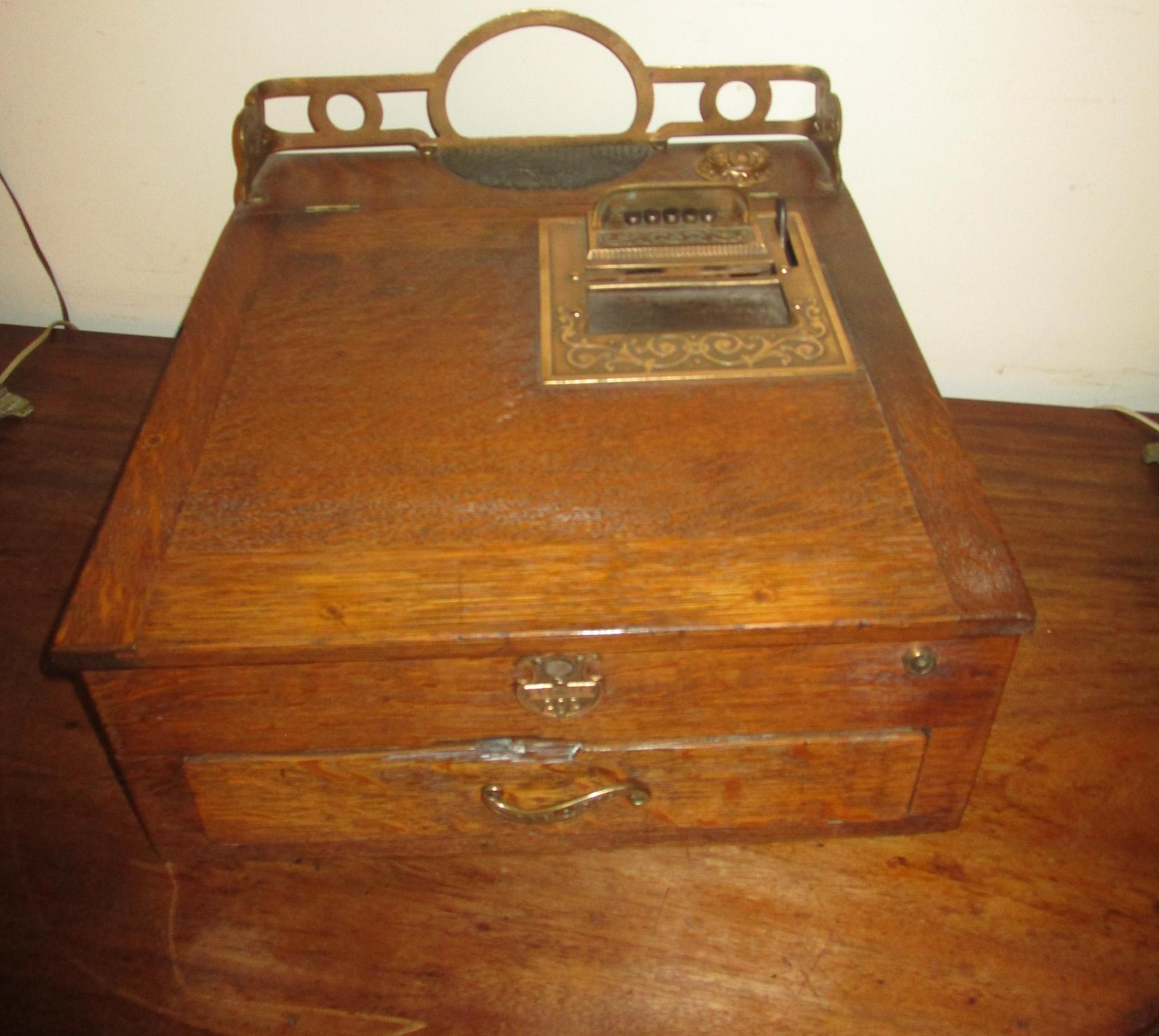 This unusual style late 19th century cash register money box was made by National Cash Register with a patent date of 1893, model number 202- 433821. Features include solid golden oak case with a covered brass inkwell, leather insert, brass gallery