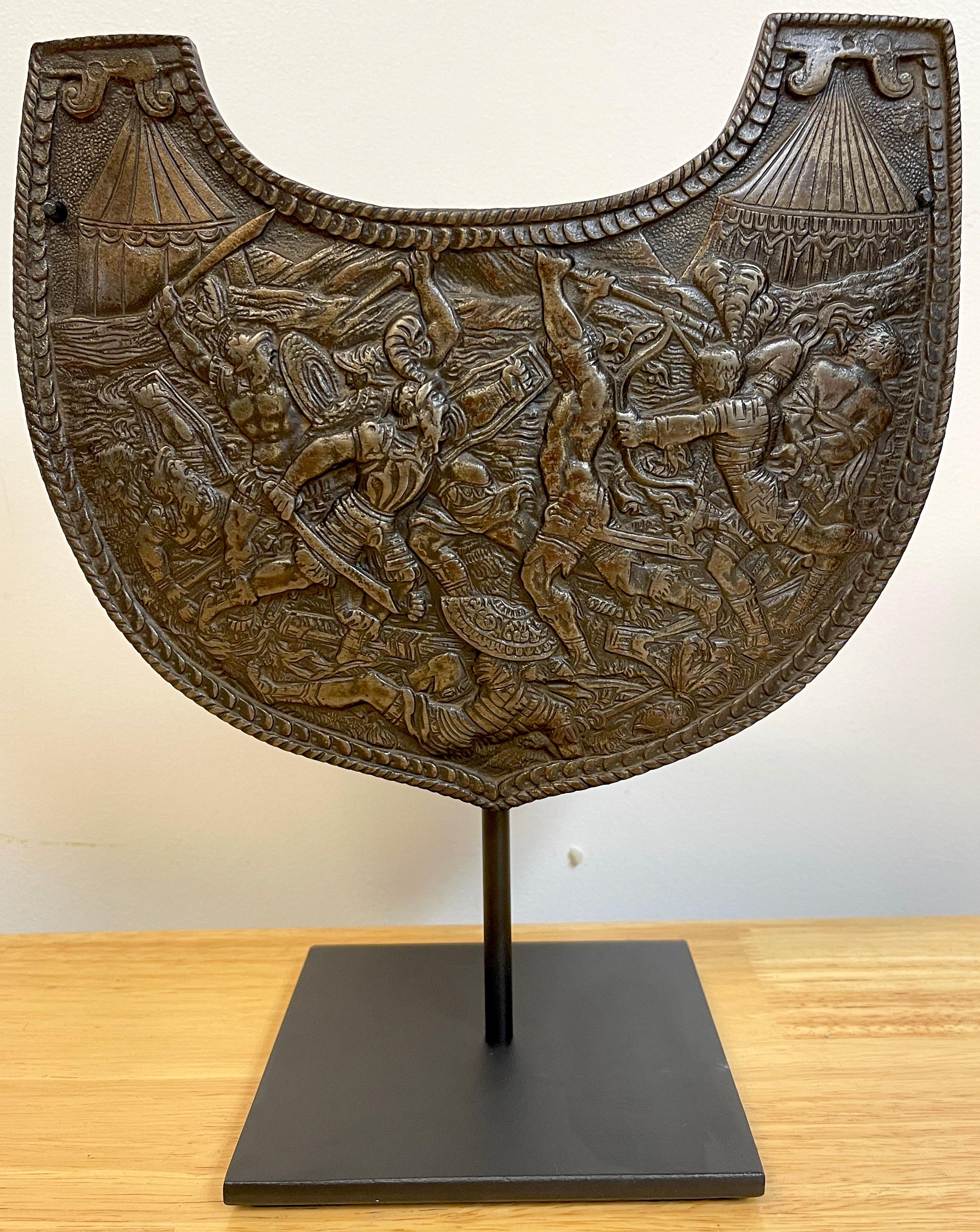 19th c Grand Tour Roman style iron gorget on stand
Decorated with a intense battle scene with Imperial Roman soldiers fighting native warriors, with two Roman Campaign tents in landscape. Museum mounted on a ebonized iron stand. 
Gorget alone 10-