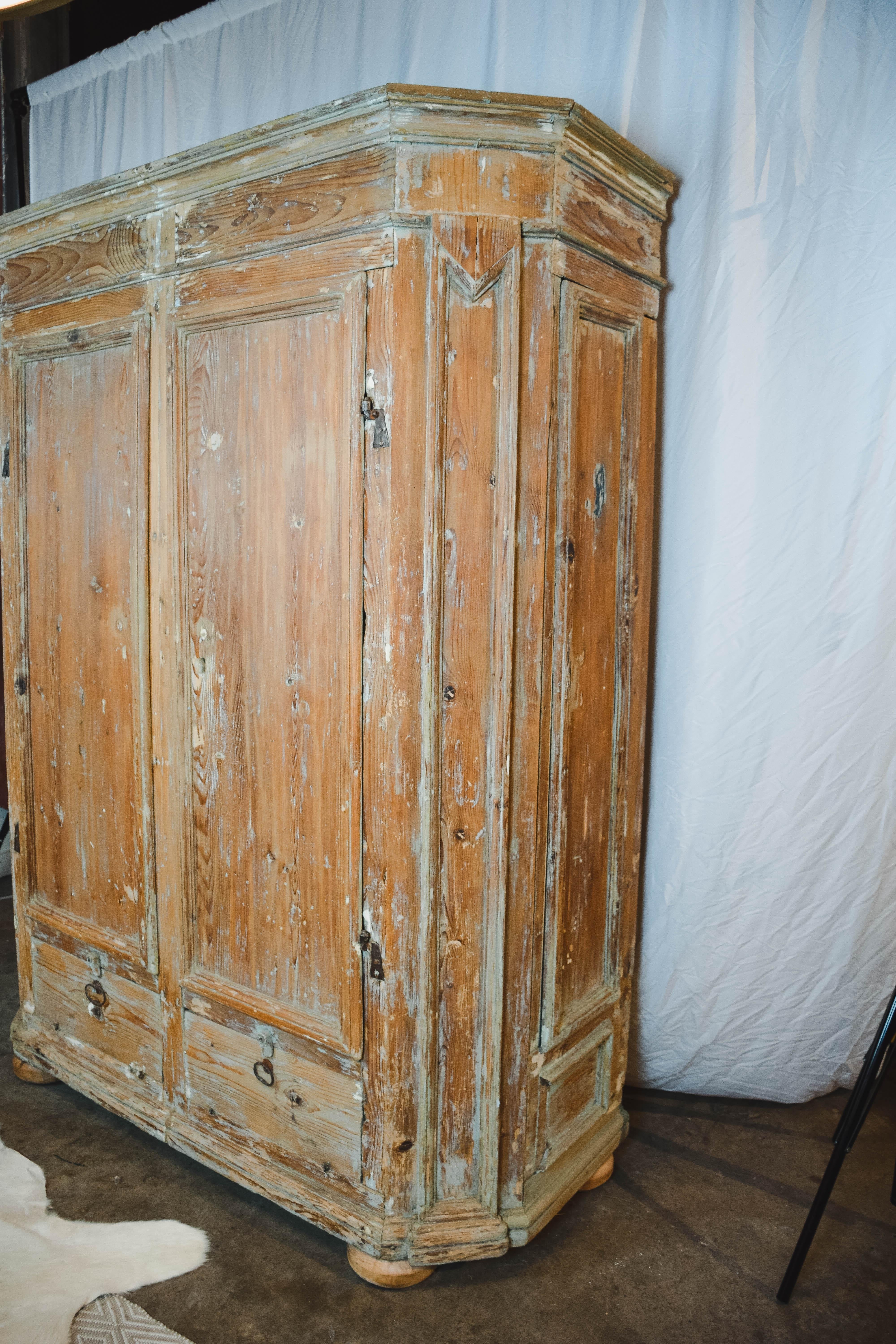 This 19th century Swedish armoire was handcrafted from solid pine, and features two large doors over two lower doors with hand forged pulls. The two lower doors appear to be drawers, however they lift up on hinges. The wardrobe has tailored molding