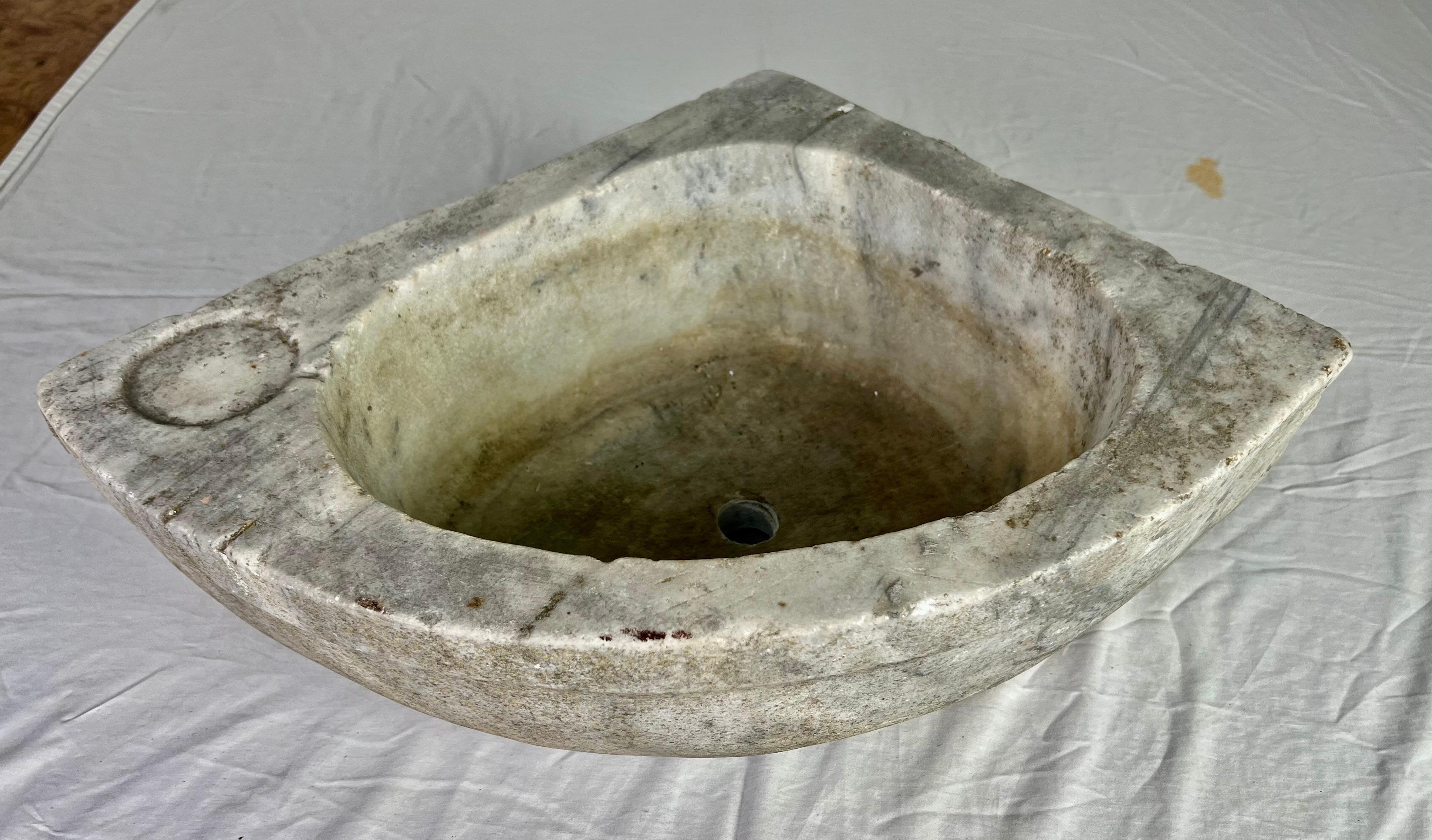 Piedra básica cincelada a mano con aspecto rústico.  La pila está tallada en una sola pieza de mármol.  El lavabo tiene forma triangular, por lo que cabe en una esquina del cuarto de baño.  Los bordes son gruesos y están toscamente acabados, por lo