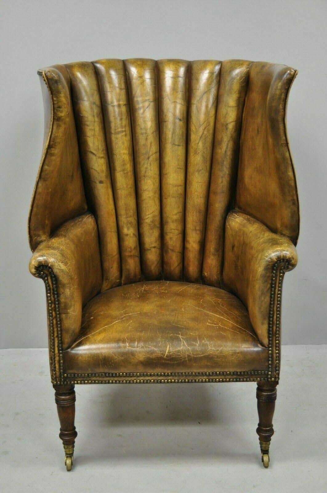 Antique 19th century Howard & Sons Ltd English brown leather channel back wingback library chair. Item features tall oversized wingback, nailhead trim, oakwood legs, brass rolling casters, beautiful original aged brown leather upholstery, solid wood
