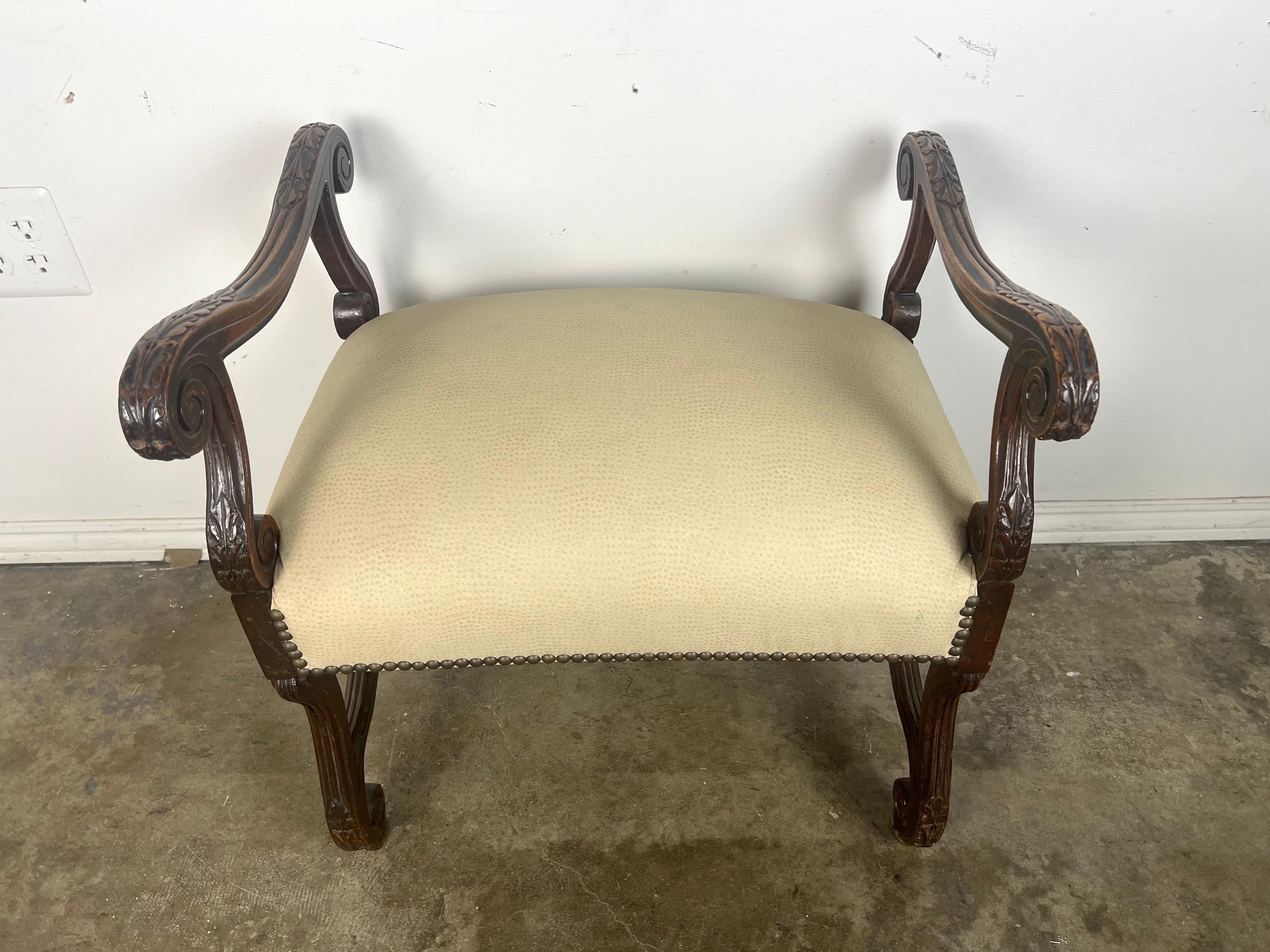 19th C. Italian Baroque style bench with a wooden frame and upholstered seat.  The frame is finely carved with decorative acanthus leaf details, especially on the legs and the arms.  The arms are gracefully scrolled, adding a touch of