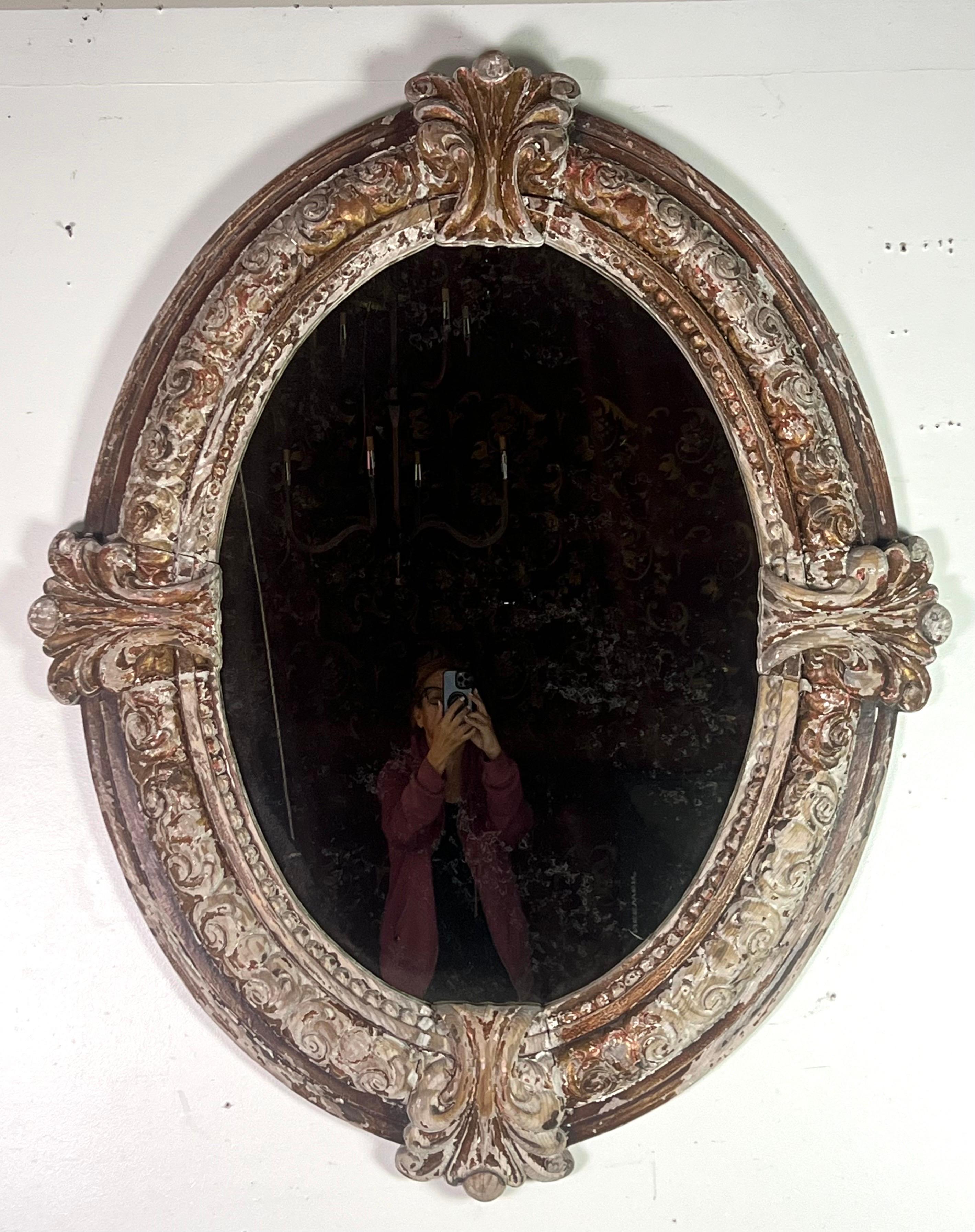 19th C. Italian Baroque style mirror with an oval shape.  The mirrors features an ornate frame made of wood with intricate carvings of scrollwork and floral motifs.  The design includes prominent flourishes at the top, bottom, land sides, with a