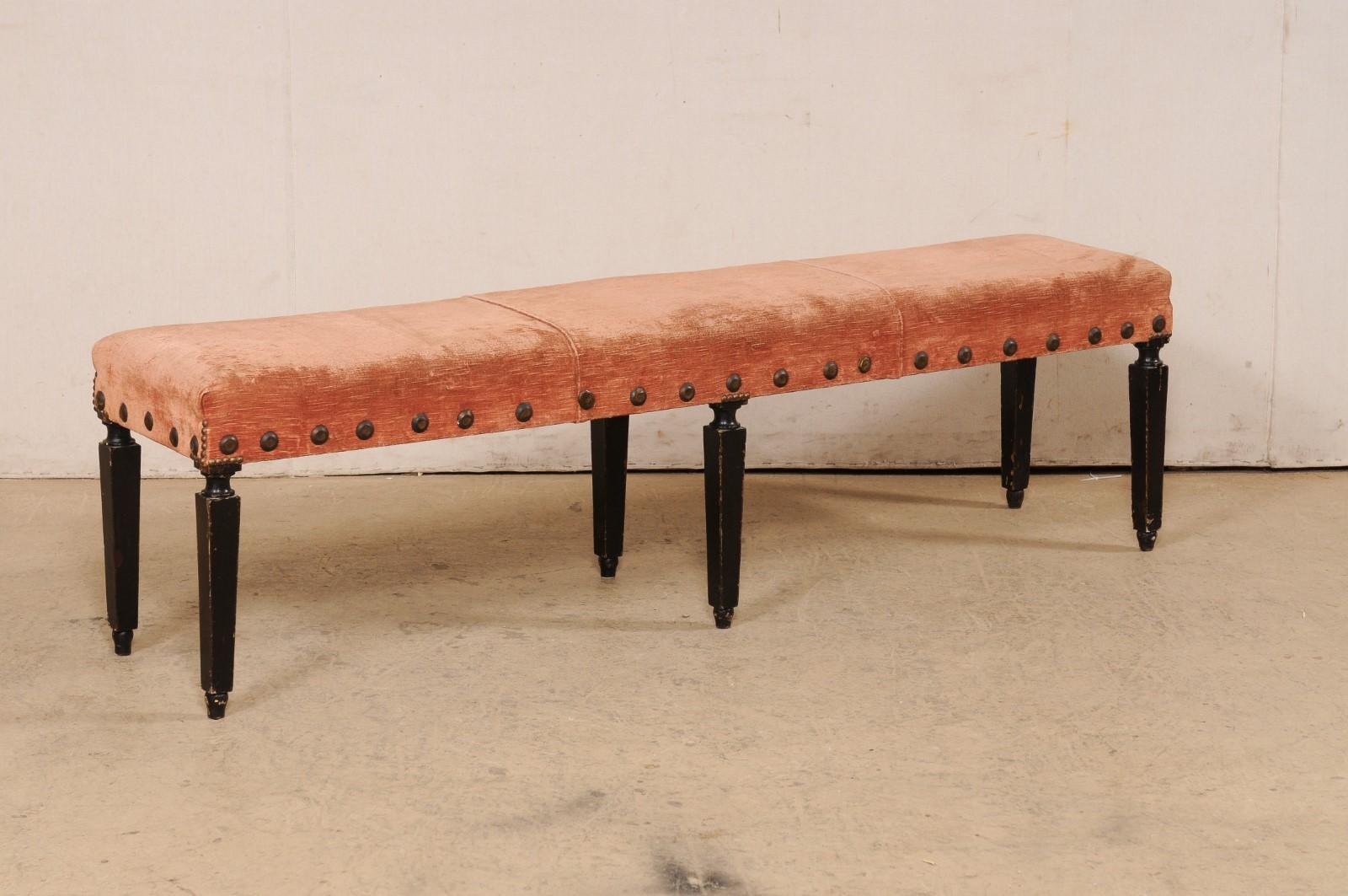 An Italian upholstered bench with carved-wood legs and large nail-head accents, 19th century. This antique from Italy, just over 5.5 feet in length, has an upholstered seat with fantastic iron nail-head accents outlining the seat rail about its