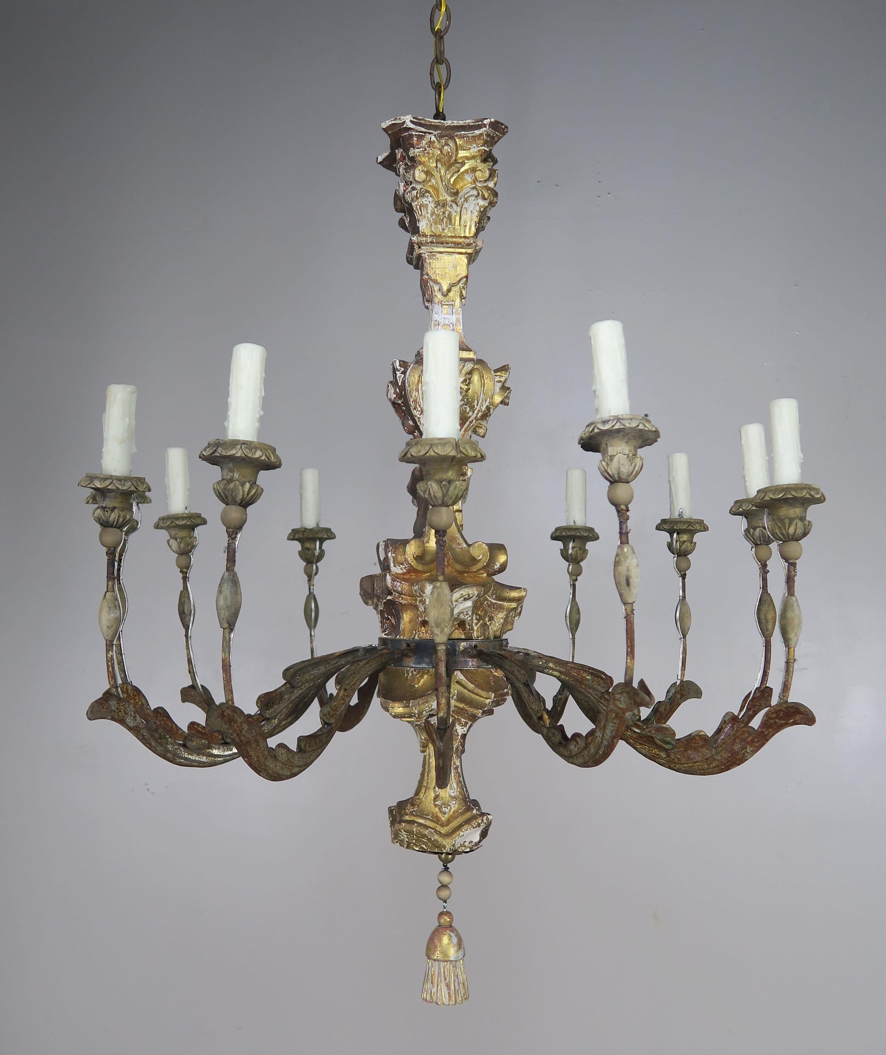 19th century Italian giltwood and iron painted chandelier. This (12) light fixture is newly rewired with drip wax candle covers. Includes chain and canopy. Giltwood tassel hanging from bottom of chandelier. Beautiful worn finish with missing paint