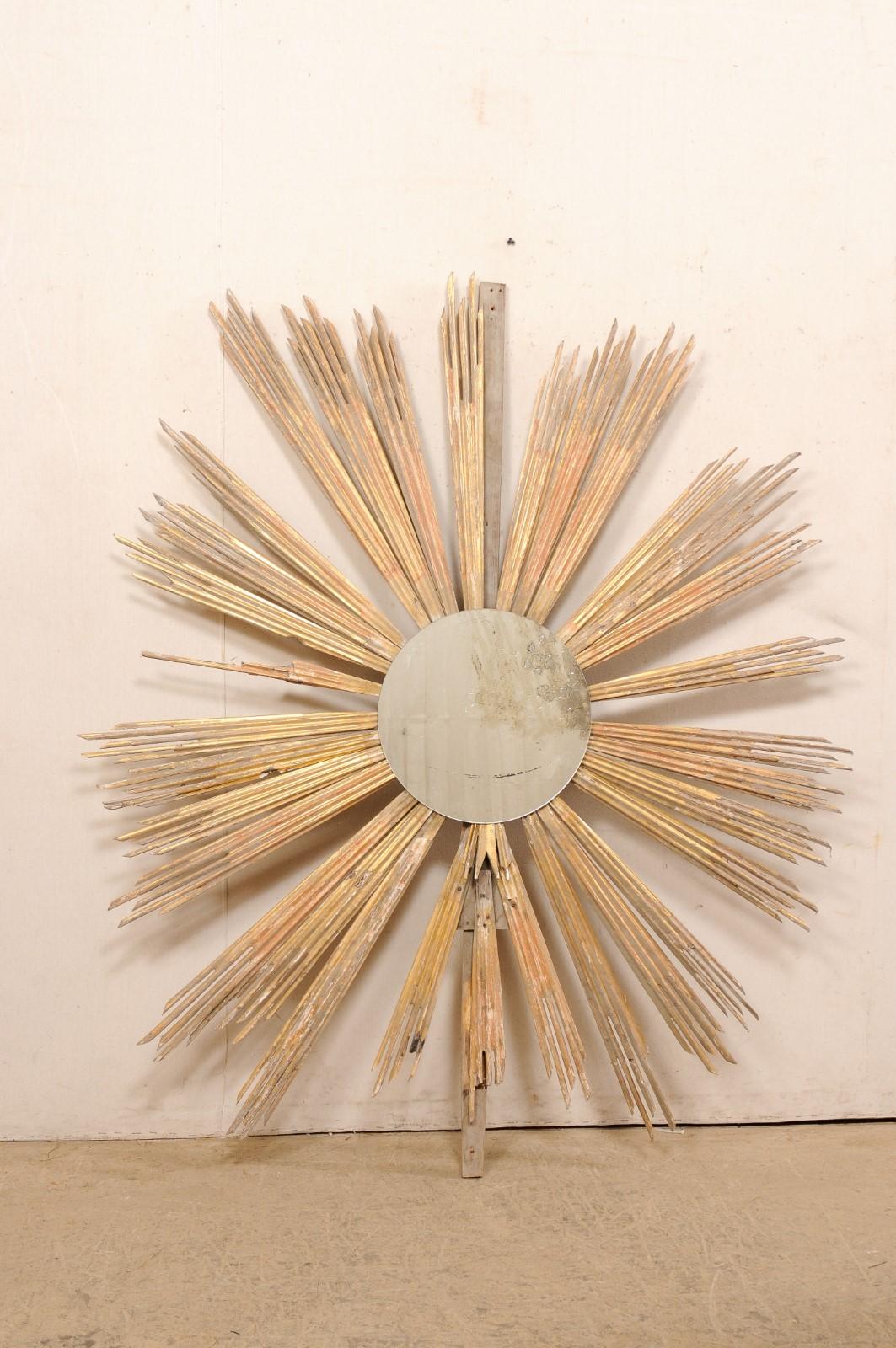An Italian large-sized gilt-wood sunburst with mirror from the 19th century. This antique wall ornament from Italy features a serious of carved-wood, gold gilt rays shooting outwardly (in undulating lengths), with a round-shaped mirror anchored