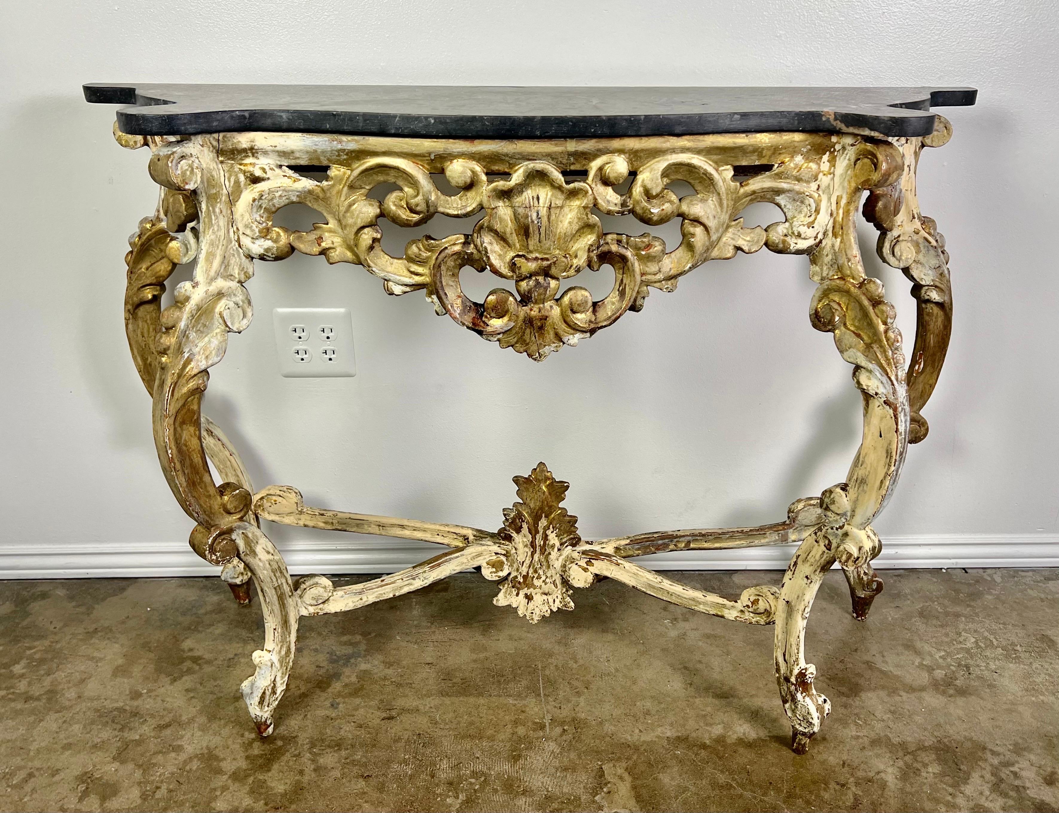 19th century Italian giltwood carved console with black marble top. The console stands on four cabriole legs with rams head feet. The scrolled legs are attached by a center stretcher that meets at a center finial. The front of the console is adorned