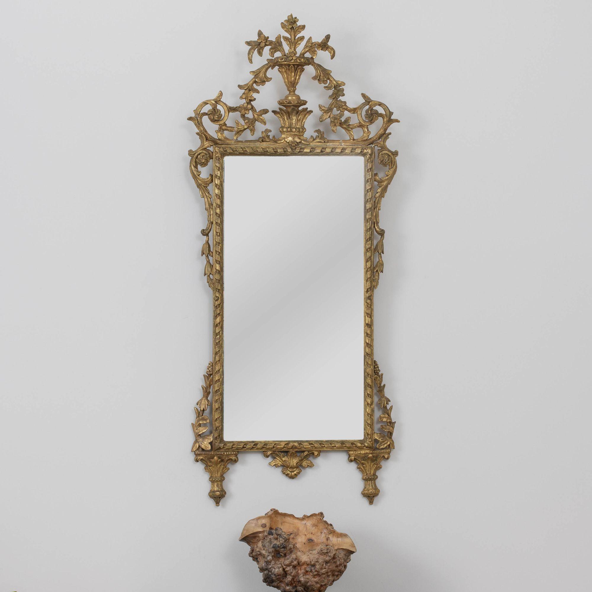 Ein eleganter, italienischer Spiegel, fein geschnitzt mit wunderschön gealtertem, originalem Vergoldungsholz und originaler Spiegelplatte. Geschnitzter Urnengiebel mit Blumen- und Blattmotiv.