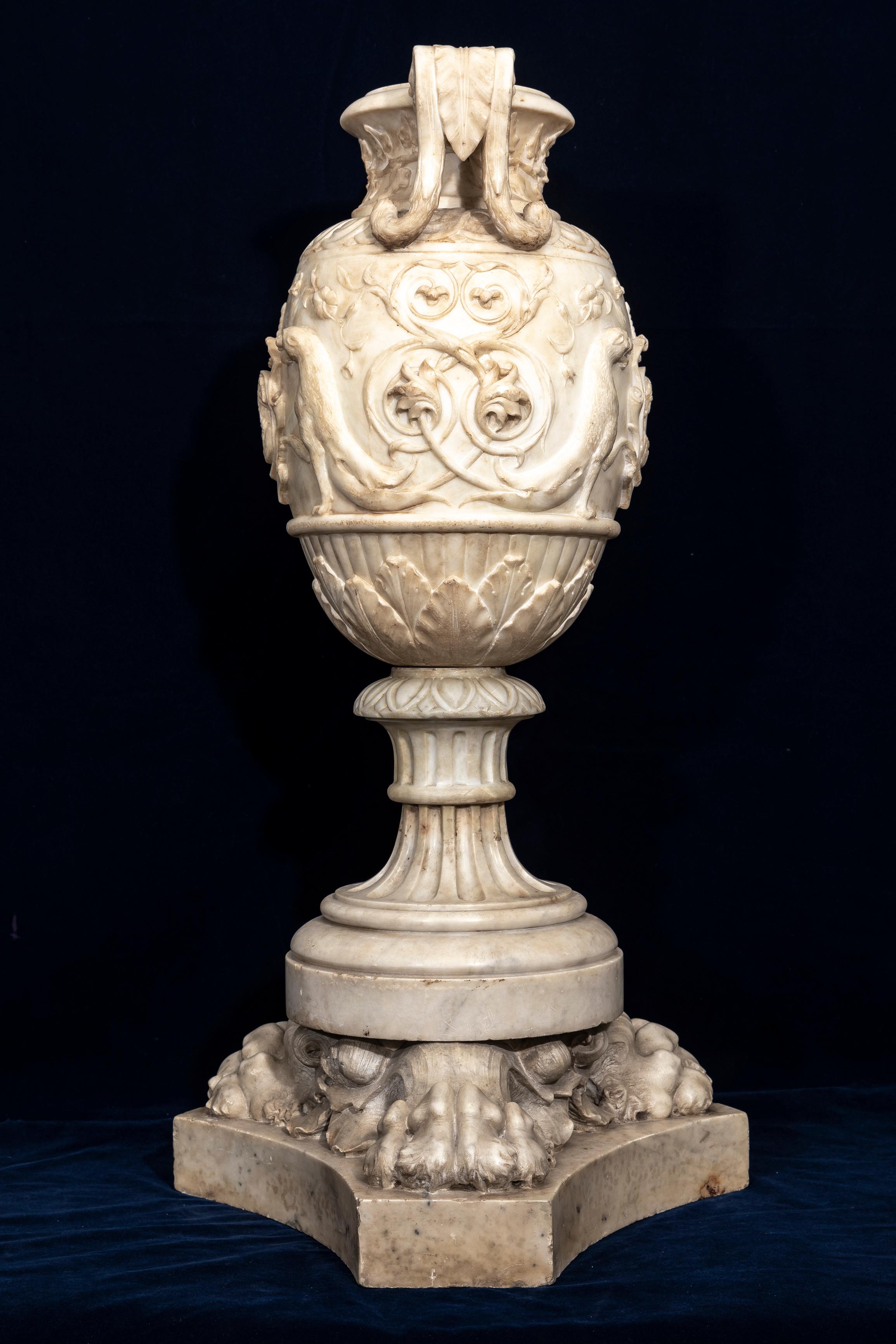 A 19th Century Italian Grand Tour Hand-Carved and Hand-Polished Carrara Marble Double-Handled Urn on Lion's Paw Base.  Intricately hand-carved with meticulous detail, the wide mouth top flows downward to a slender neck and bulbous body.  The body is