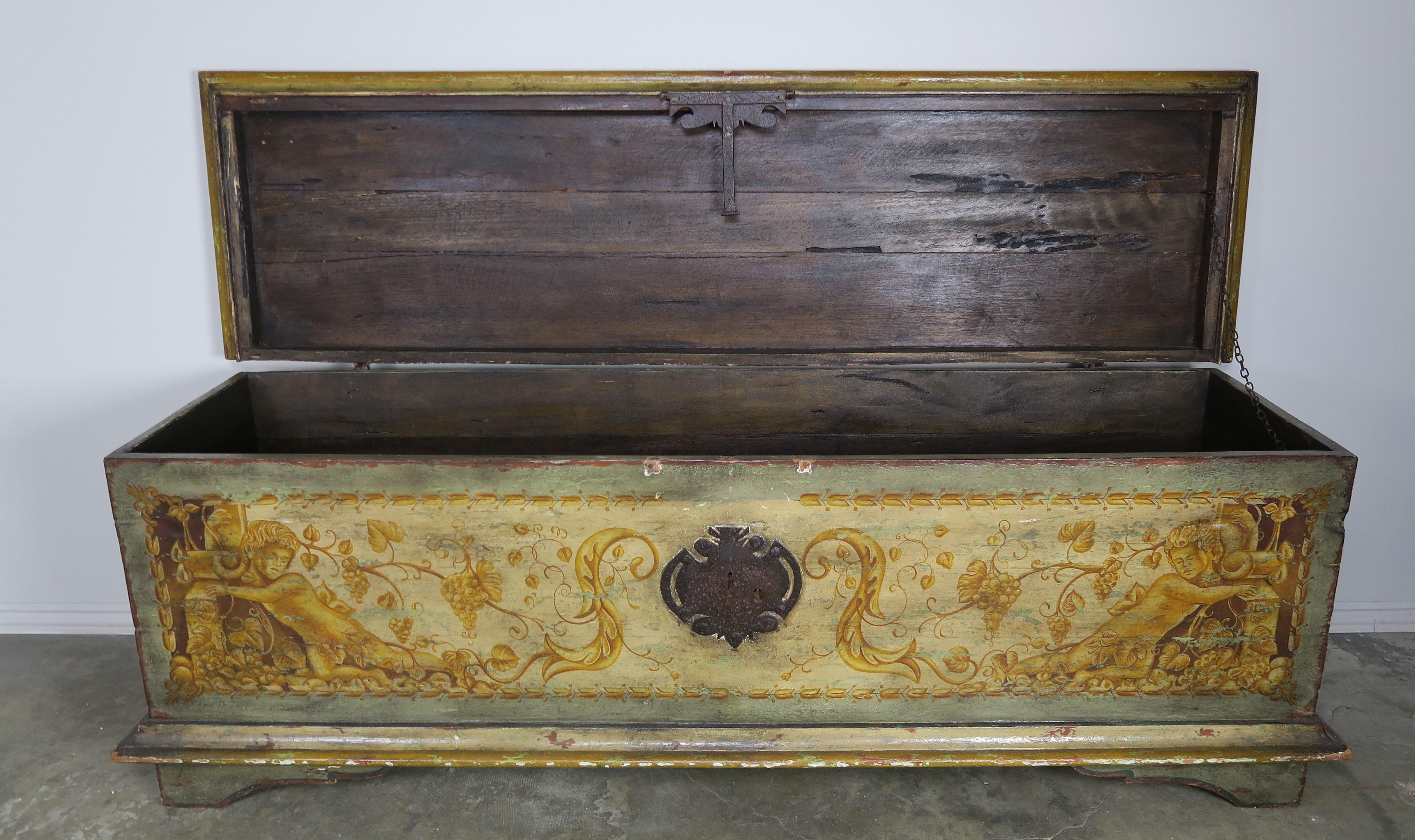 19th century Italian hand painted chest depicting a pair of cherubs leaning against a pair of torcheres and surrounded by flowers and swirling acanthus leaves throughout. Original hand wrought iron hardware.